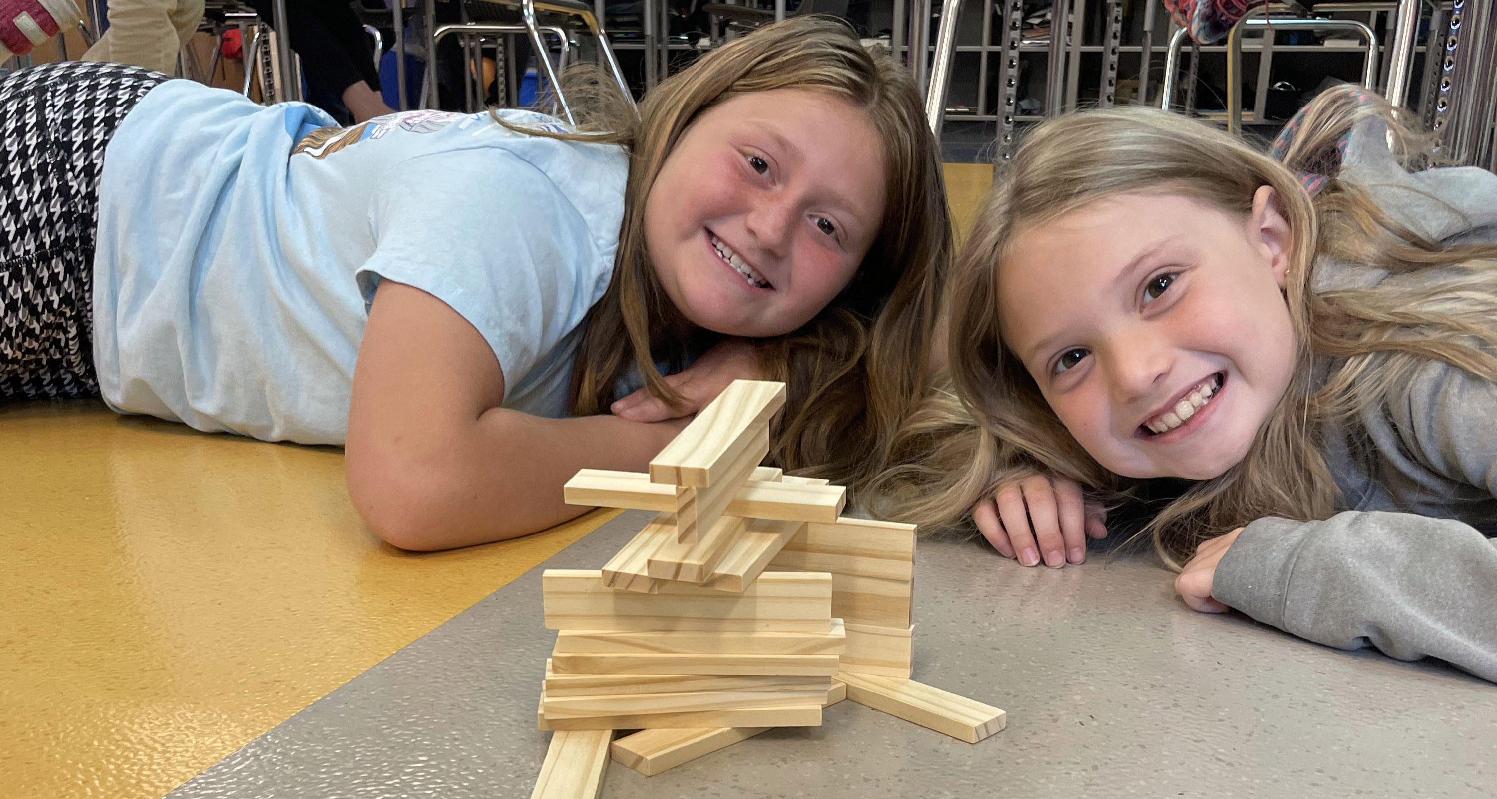 Two girls laying down in front of a stack of wooden blocks