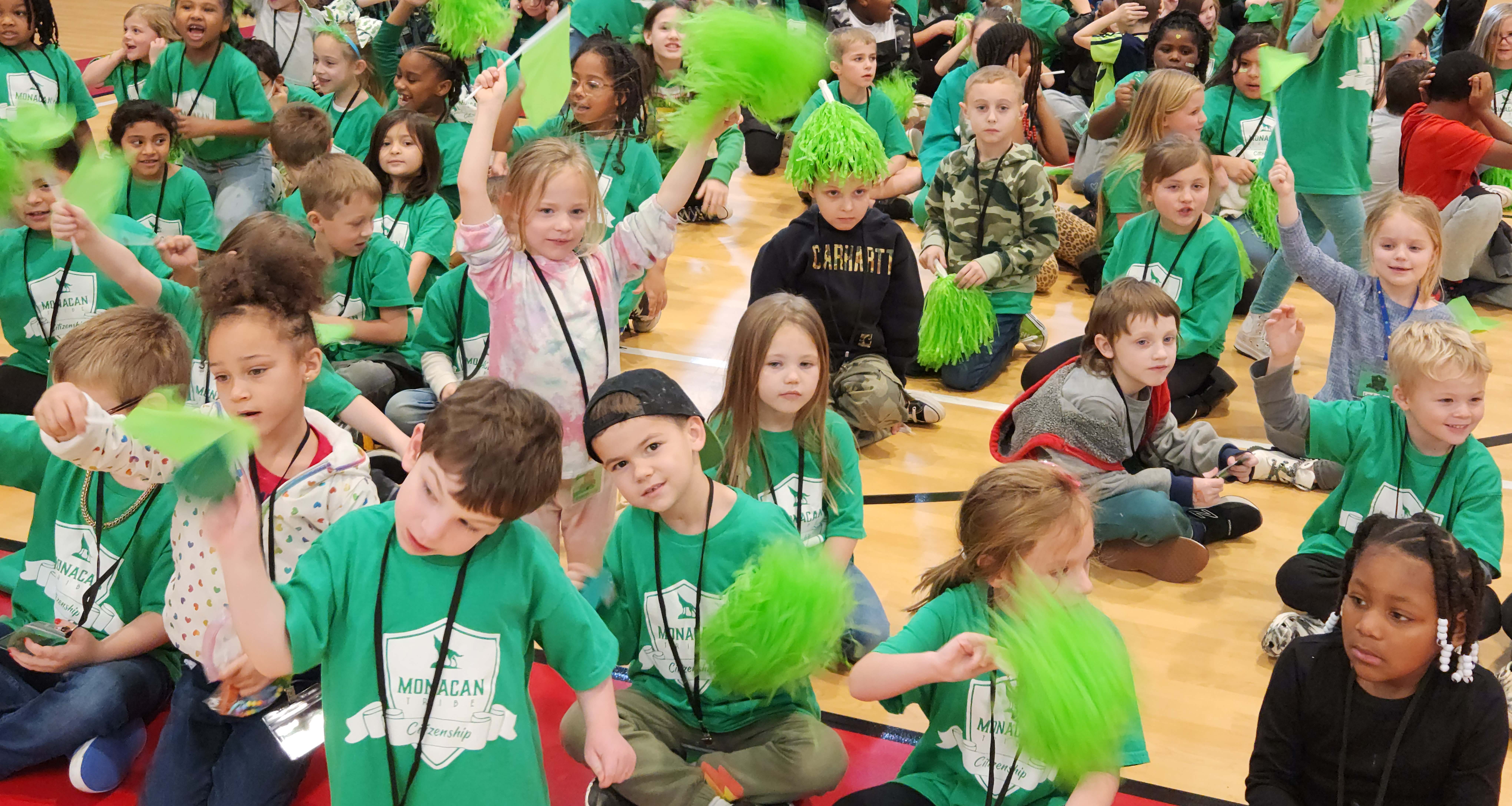 A large group of student wearing green sitting down in the cafeteria