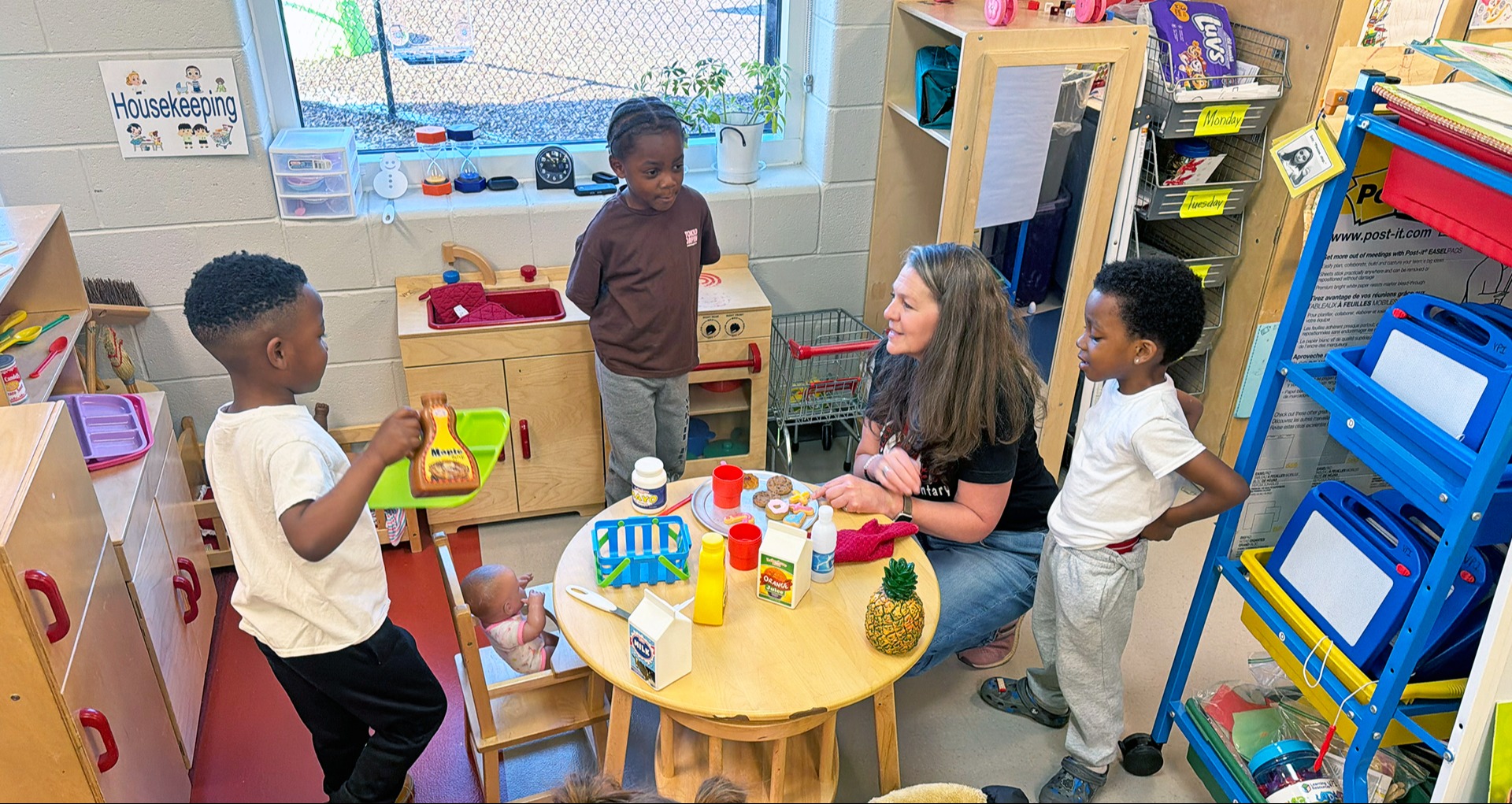 three students working ith teacher playing with food in play kitchen