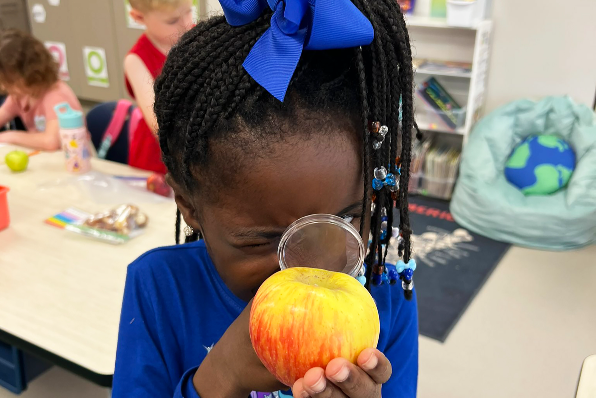 Female student studying an apple with a magnifying glass.