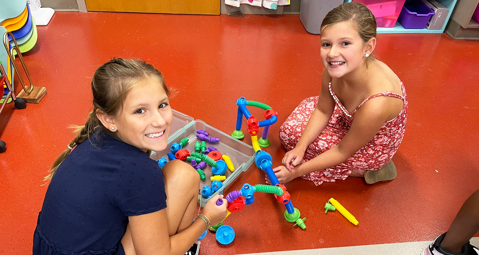 Two students sitting on the floor playing with tube blocks.