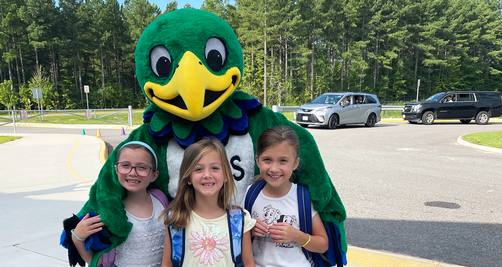 Mascot hugging three children outside.