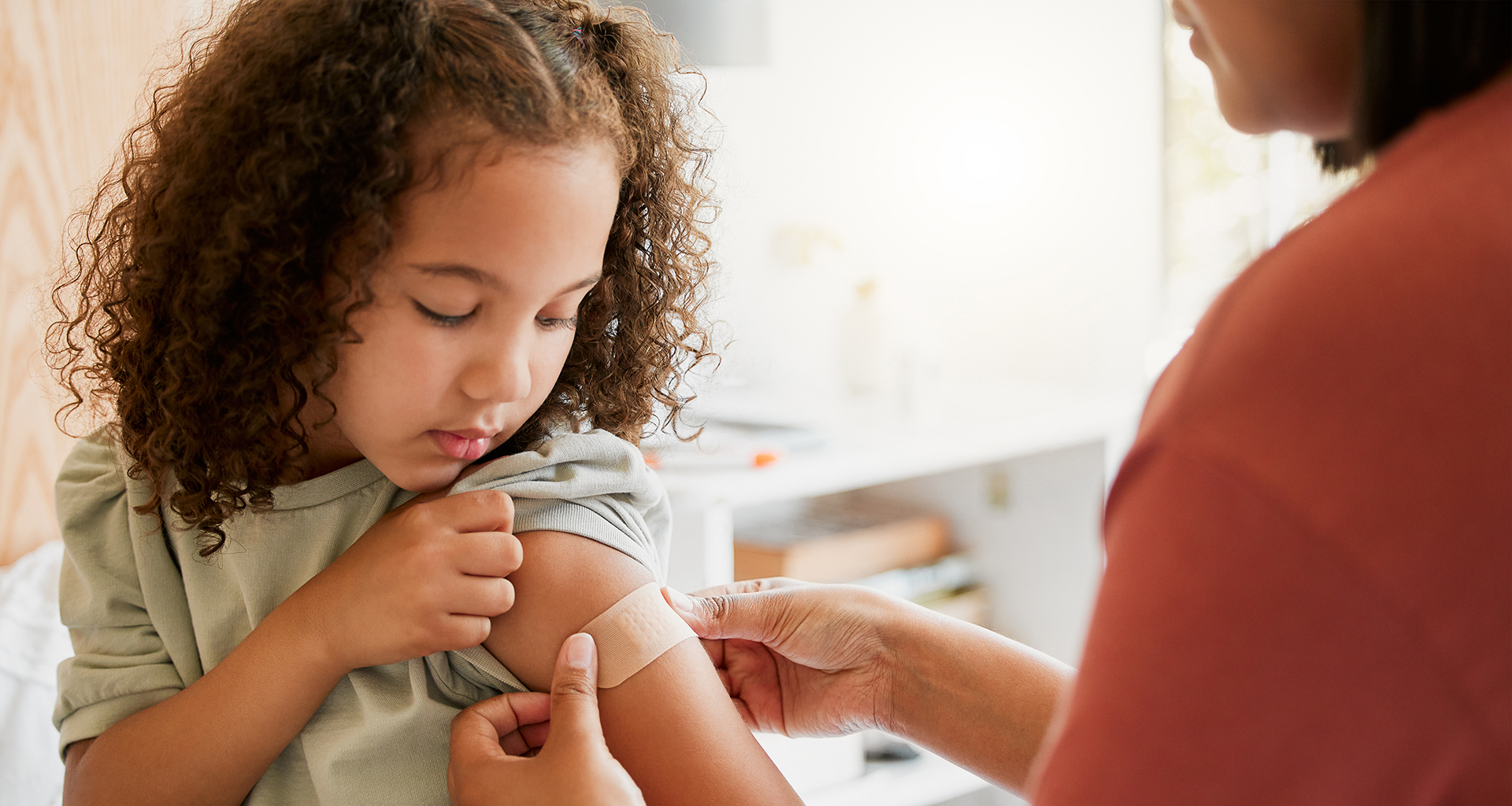 An adult putting a bandage on a girl's arm