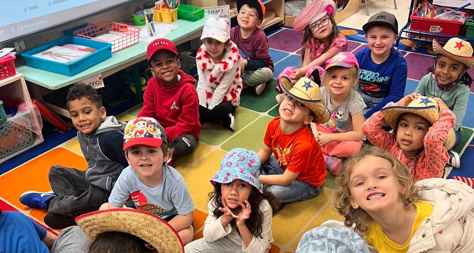 A group of kindergartners wearing hats and sitting on the carpet