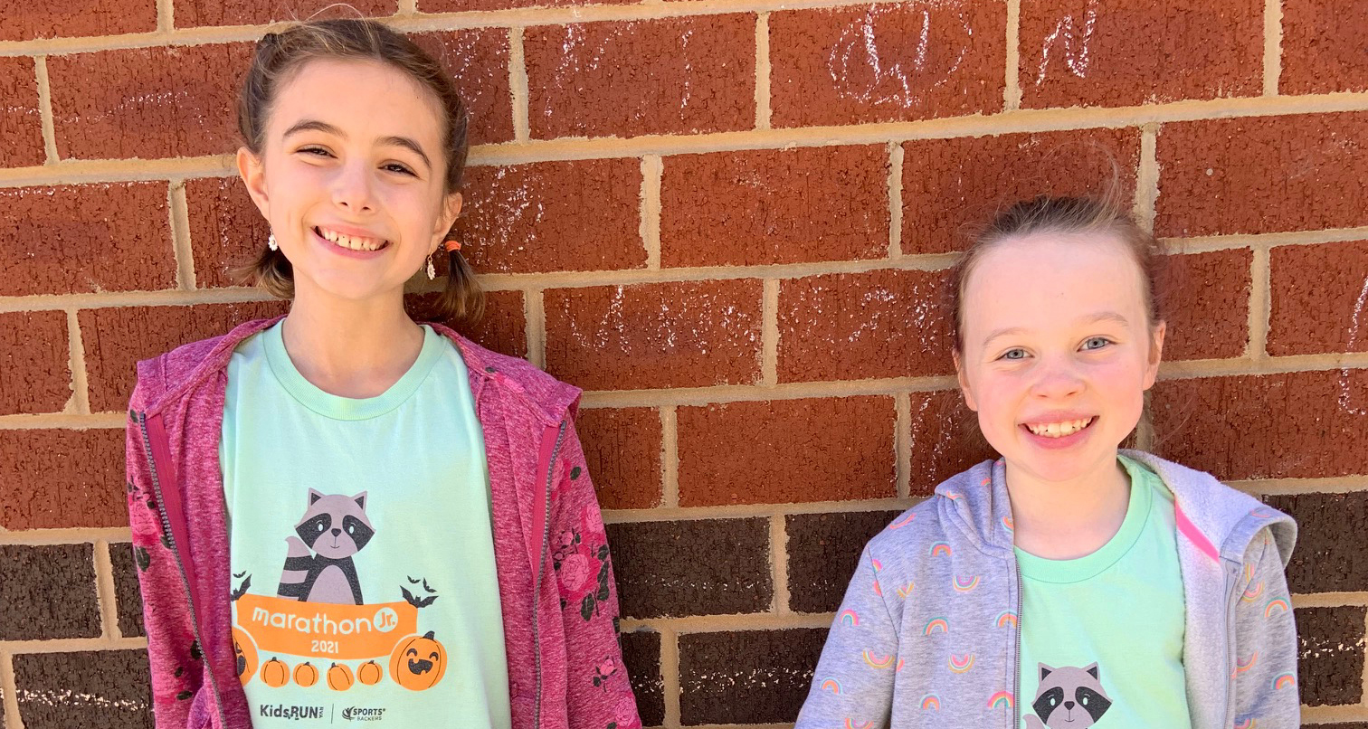 Two third graders pose for a photo in front of a brick wall