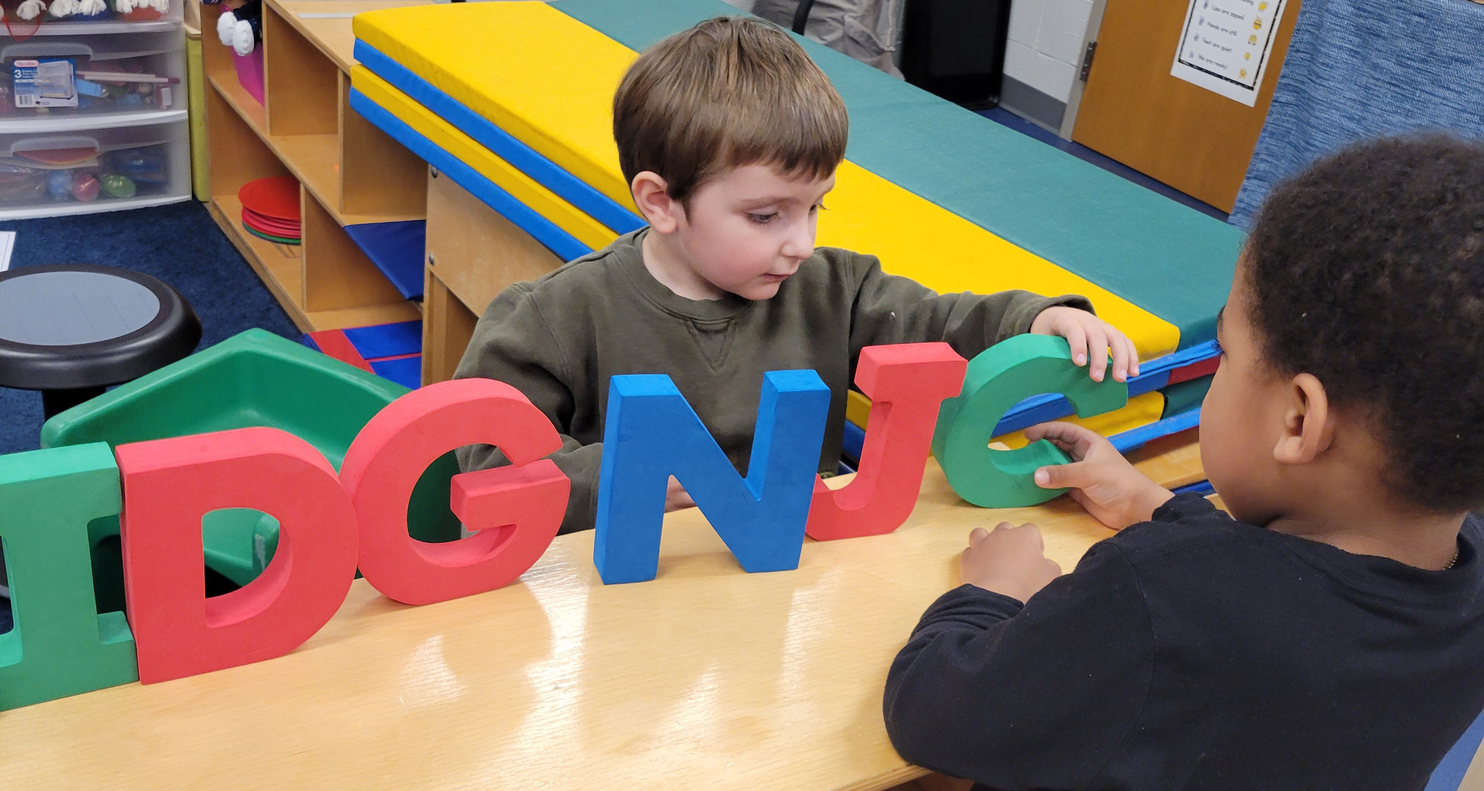 Two students playing with large plastic letters in class
