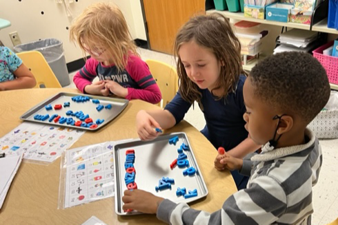 Three students working on the alphabet at their table.