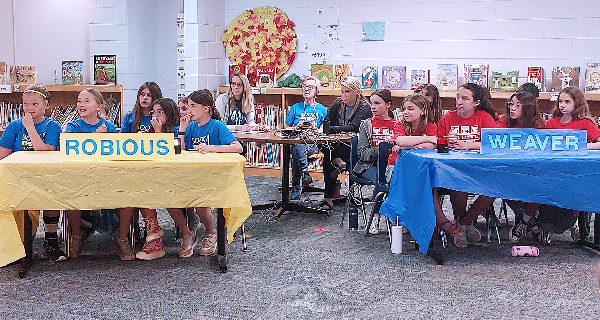 Battle of the books in the library. Two tables with students sitting at them.