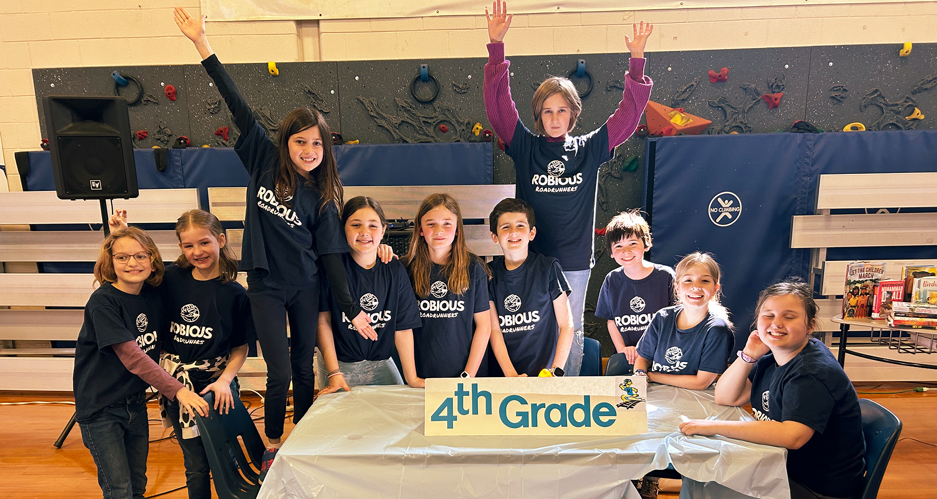Students at a table with a fourth grade sign pose for a photo.