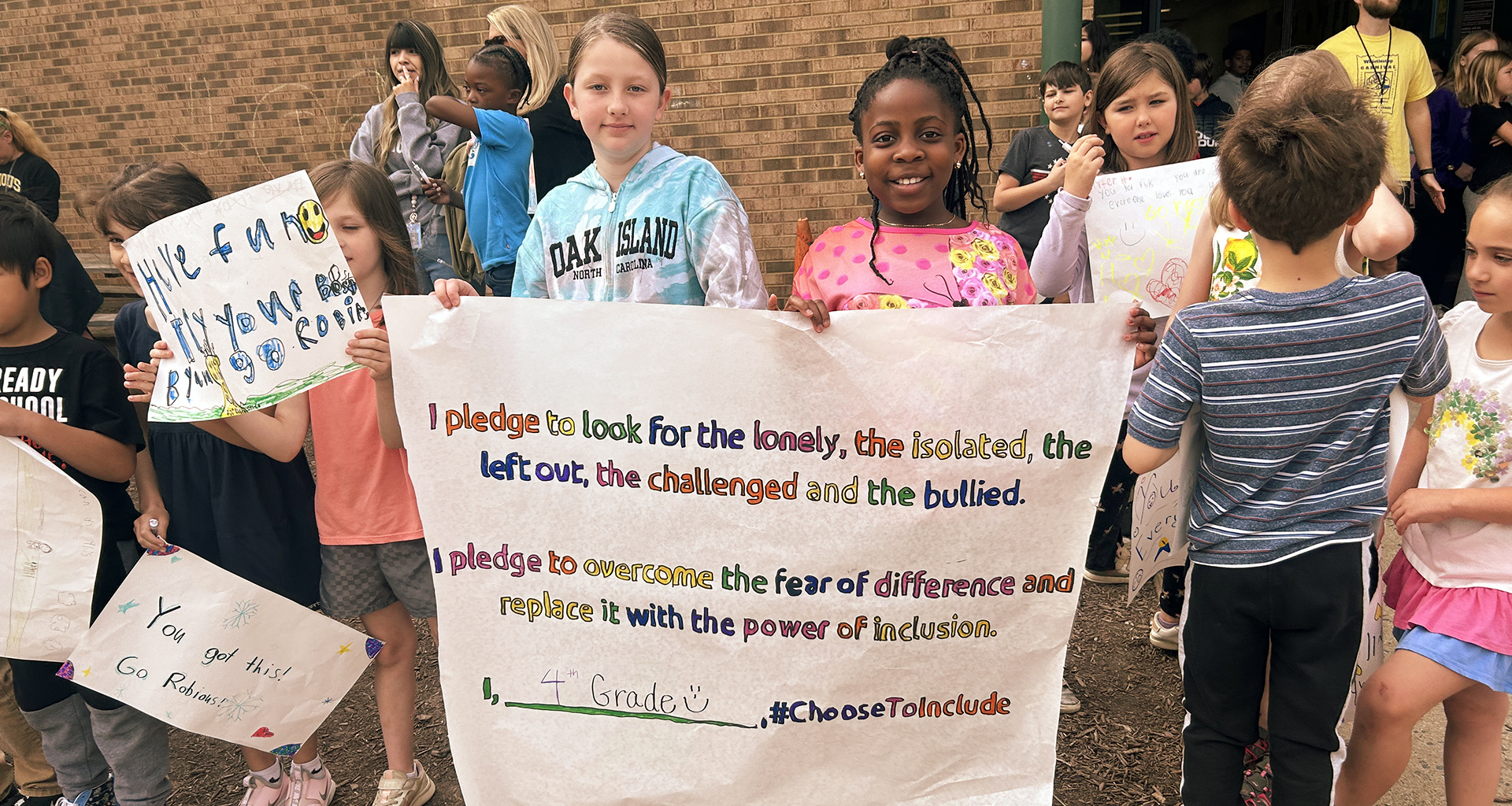Students outside holding up signs that pledge to be kind