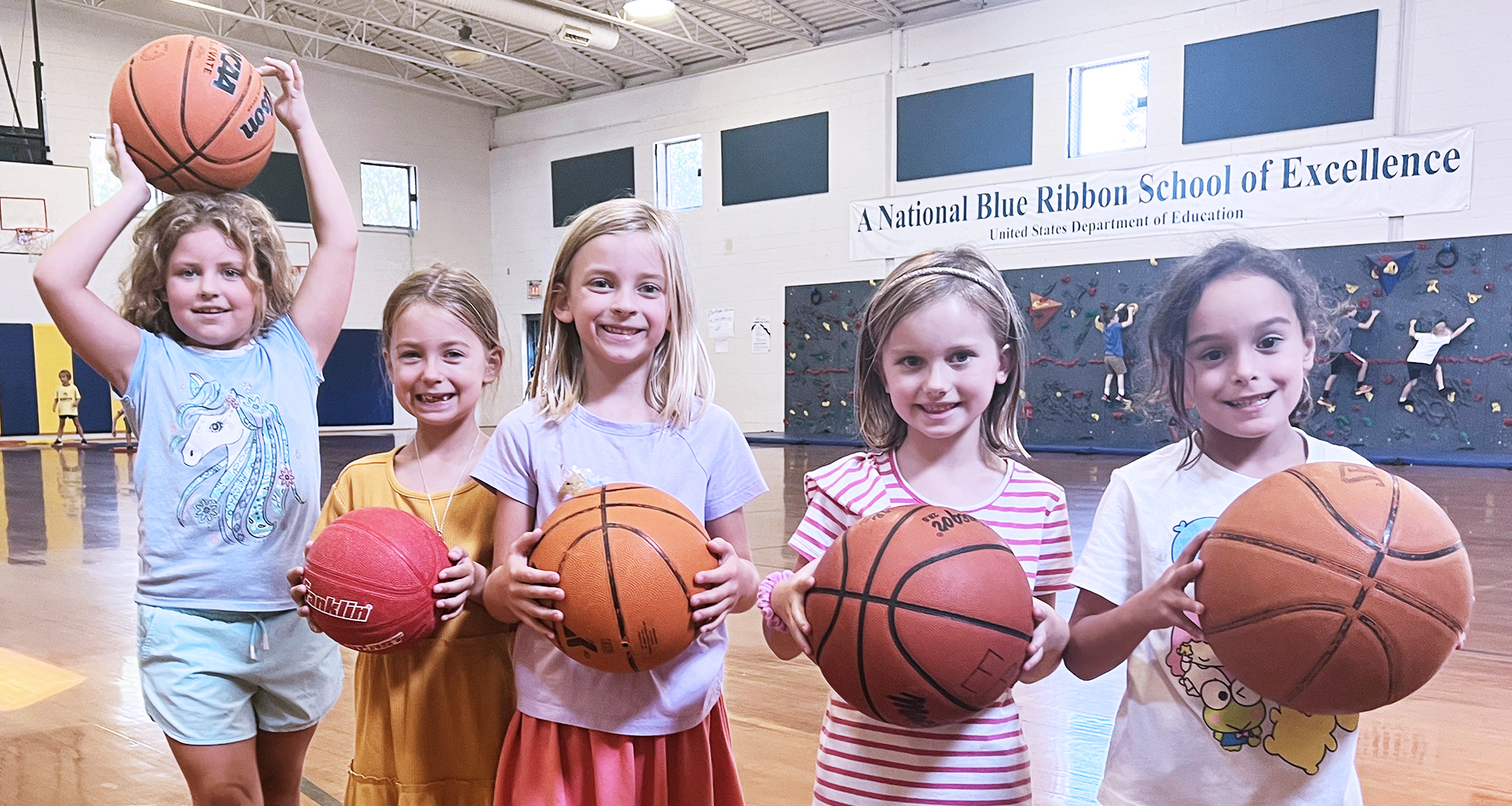 Five girls holding basketballs in the gym.