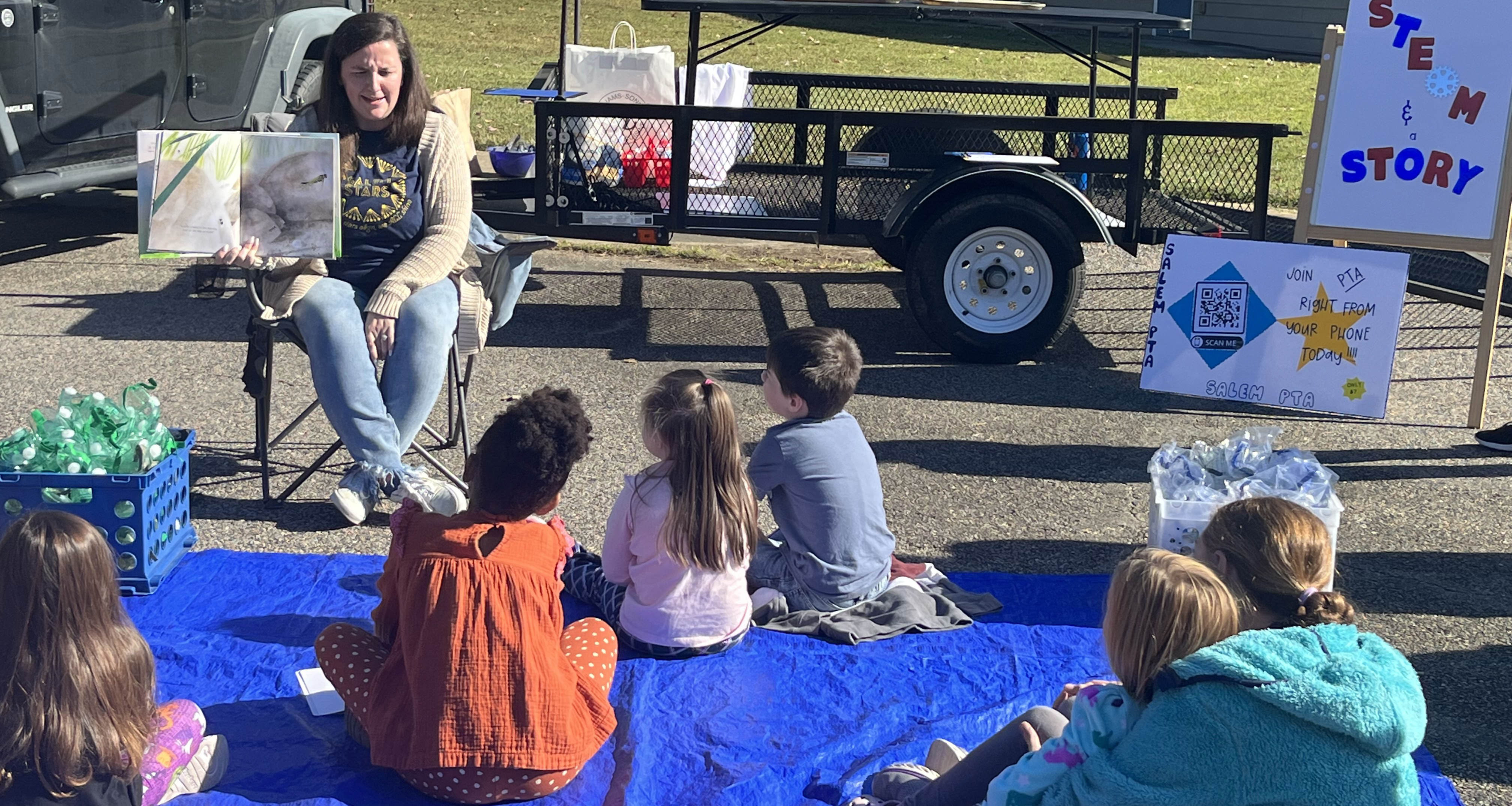 A volunteer is reading a book to a group of students outside
