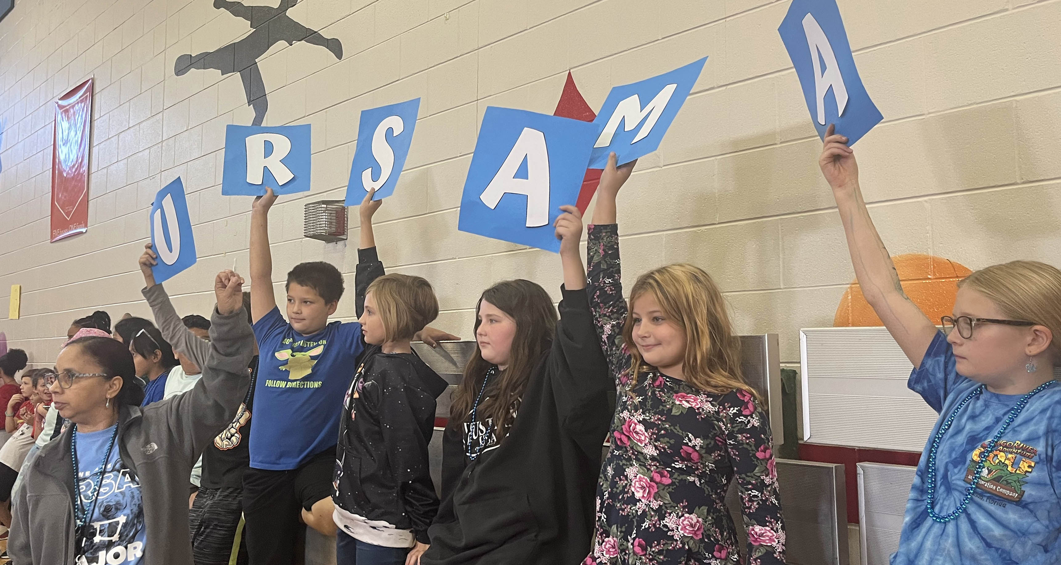 A group of students holding large letters in the gymnasium