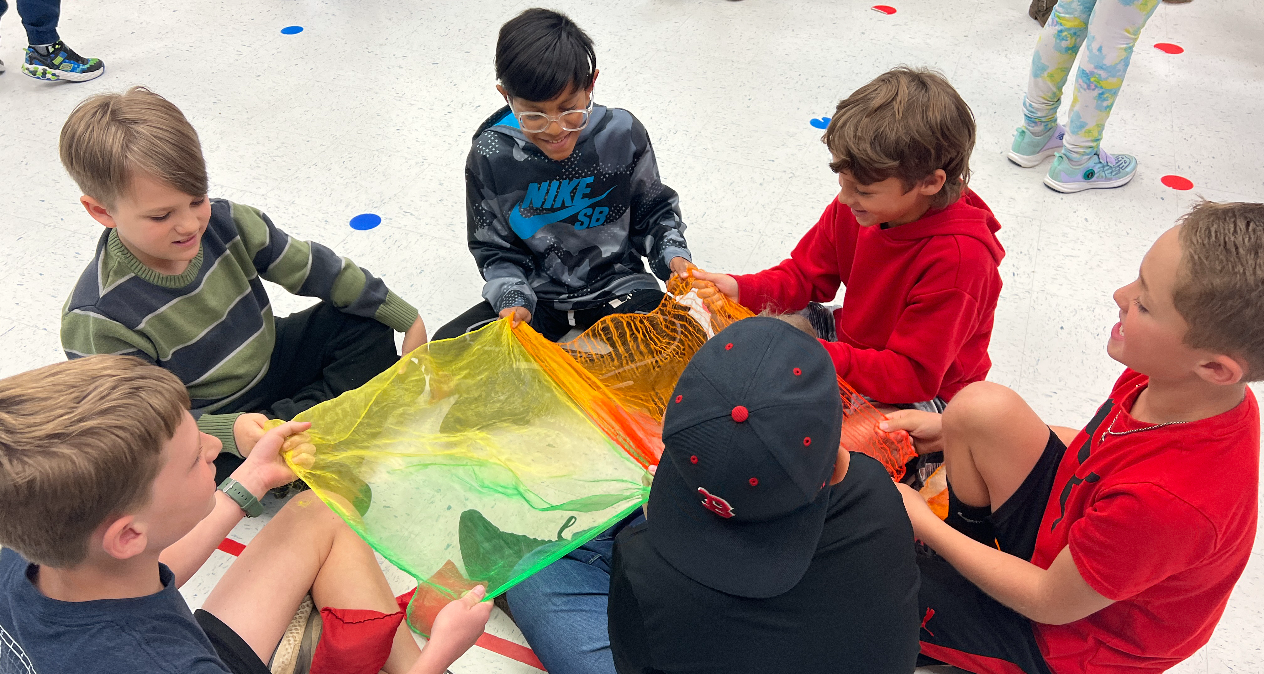 A group of six students playing with rainbow colored cloth