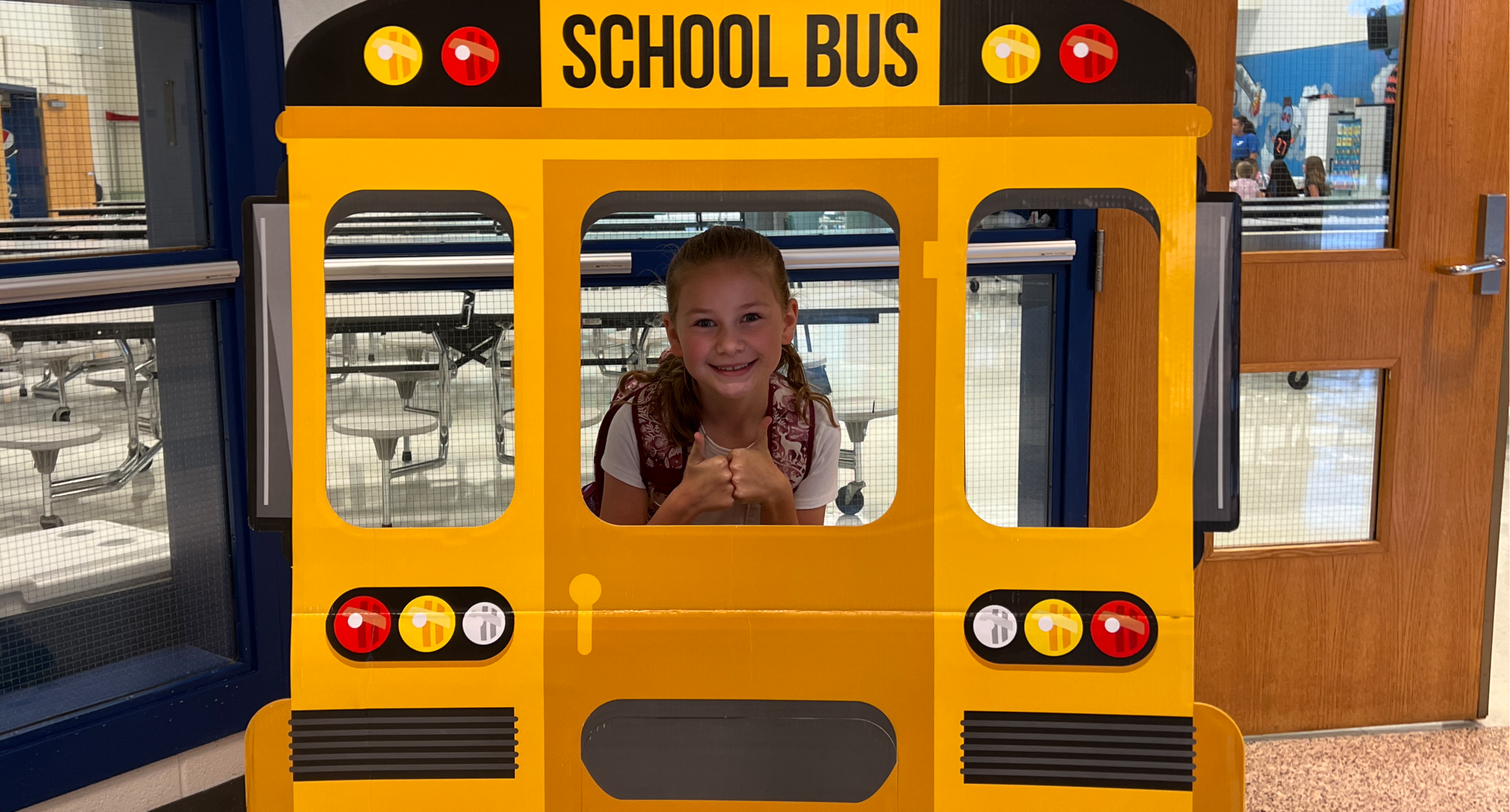 A young girl behind a photo prop of a school bus