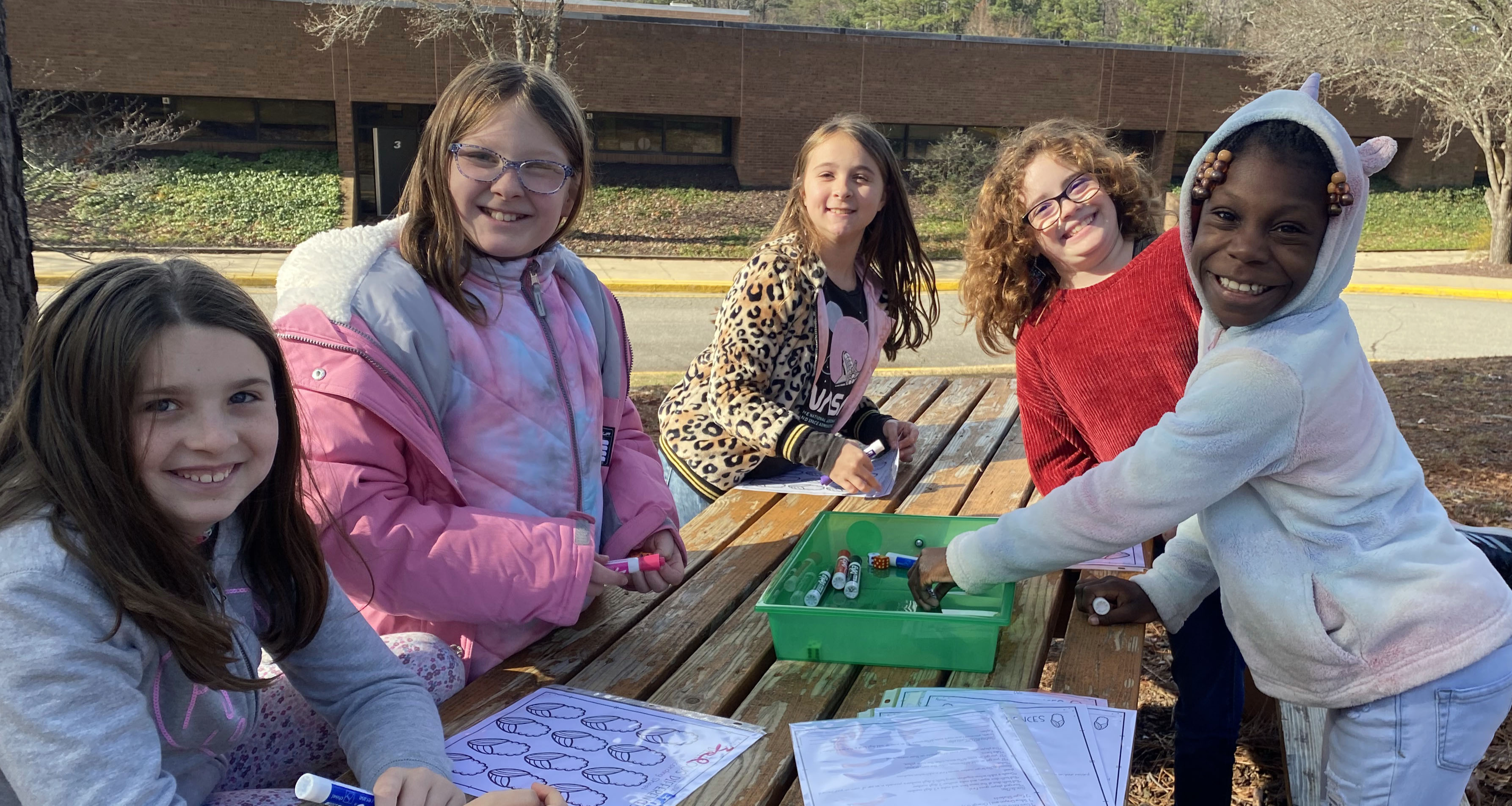 Five students color outside on a picnic table