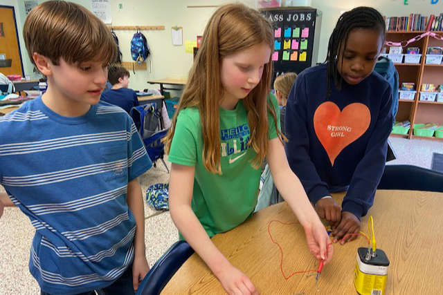 Three students working on a project using a battery