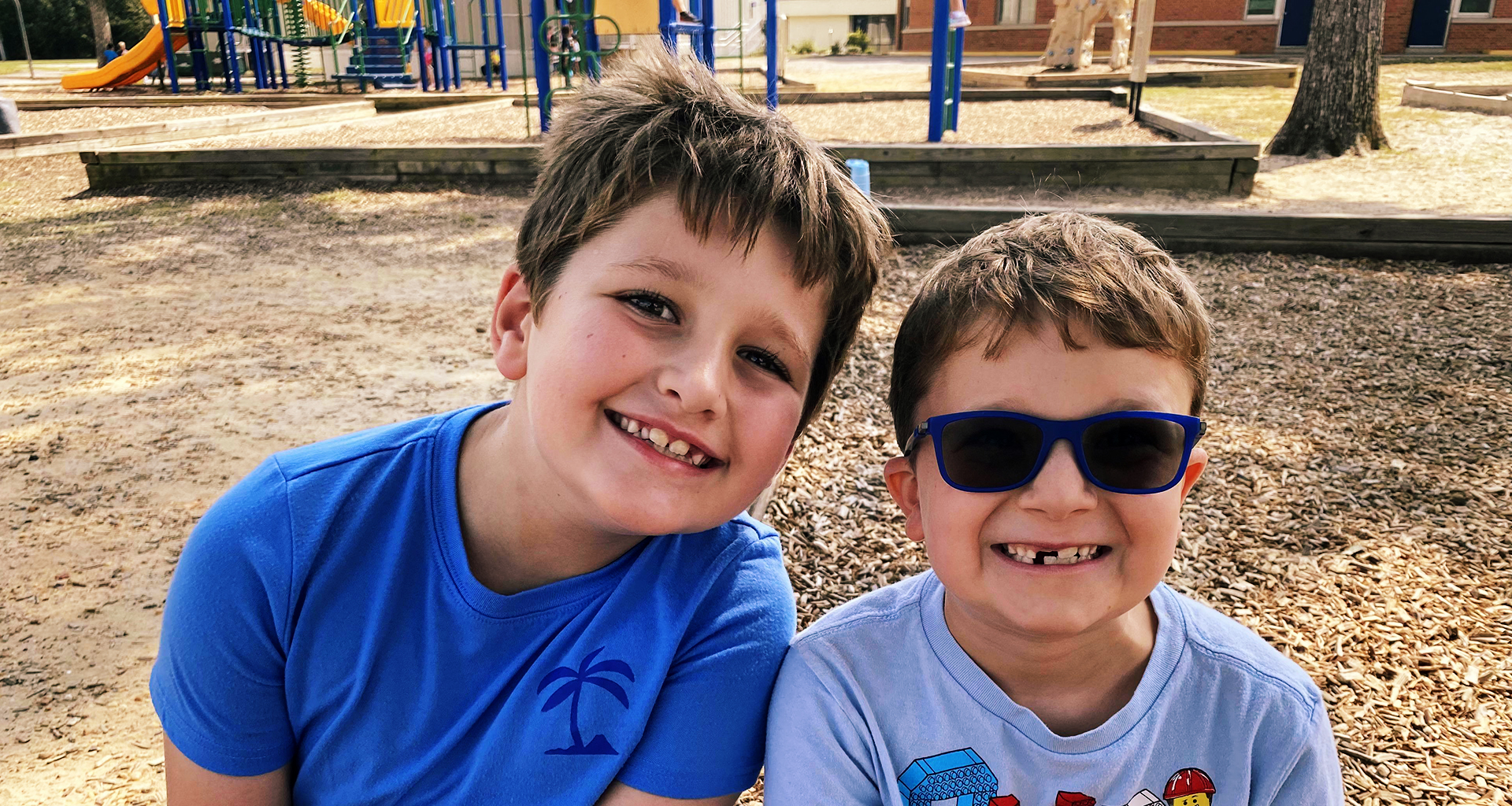 Two students smiling as they sit in front of the playground