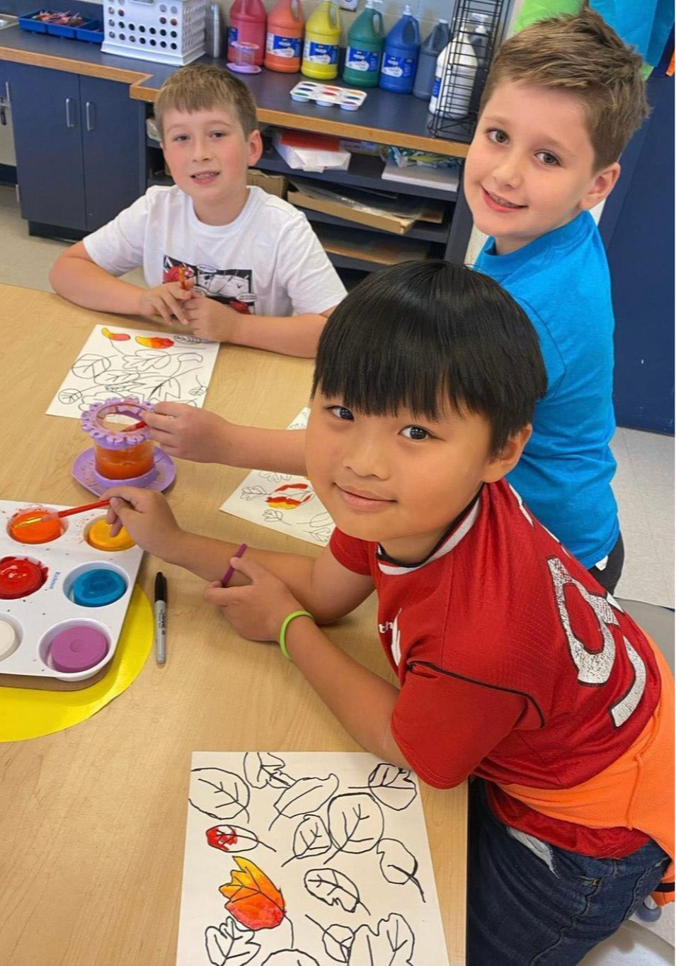 Three student coloring in art class with paint