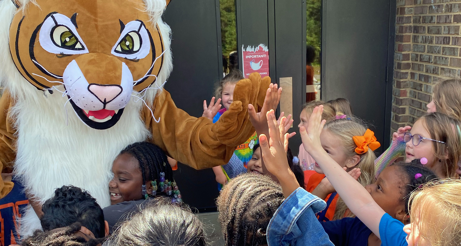 Students high-five the mascot outside.