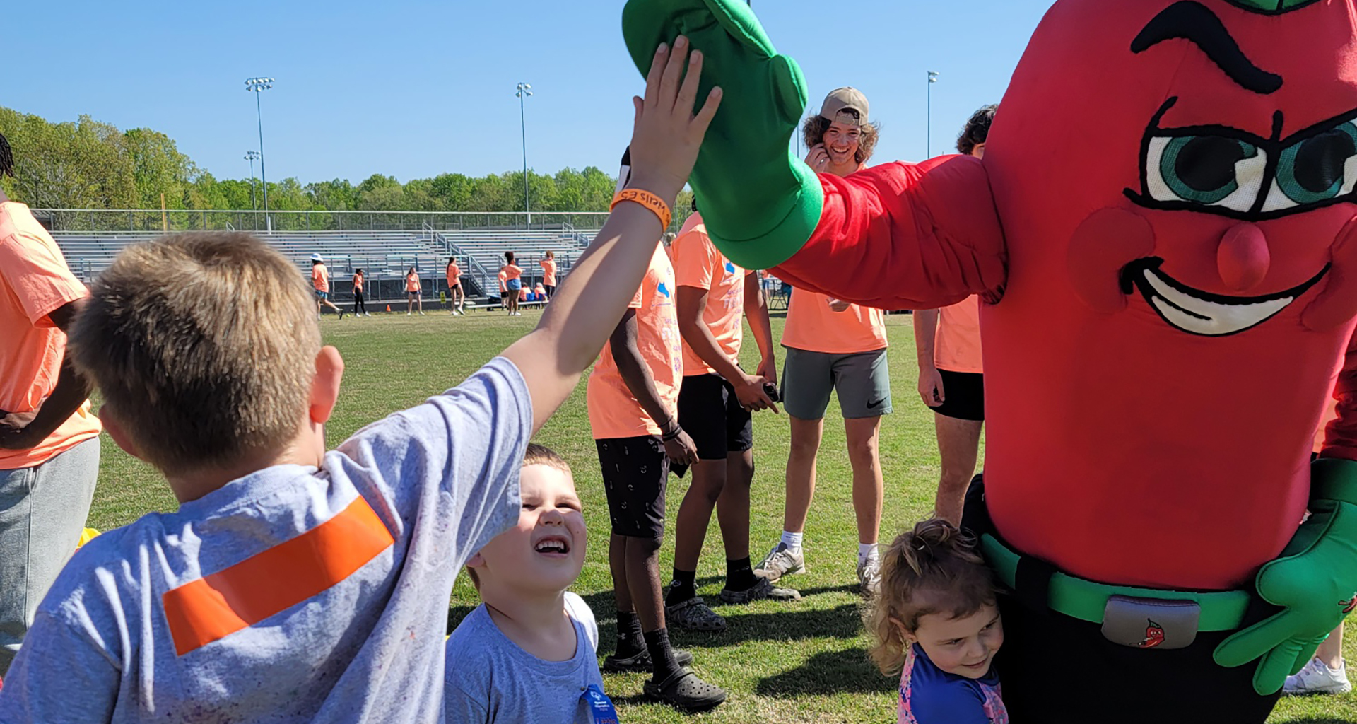 One student hugs and one student high-fives the mascot at an outdoor Olympic activity