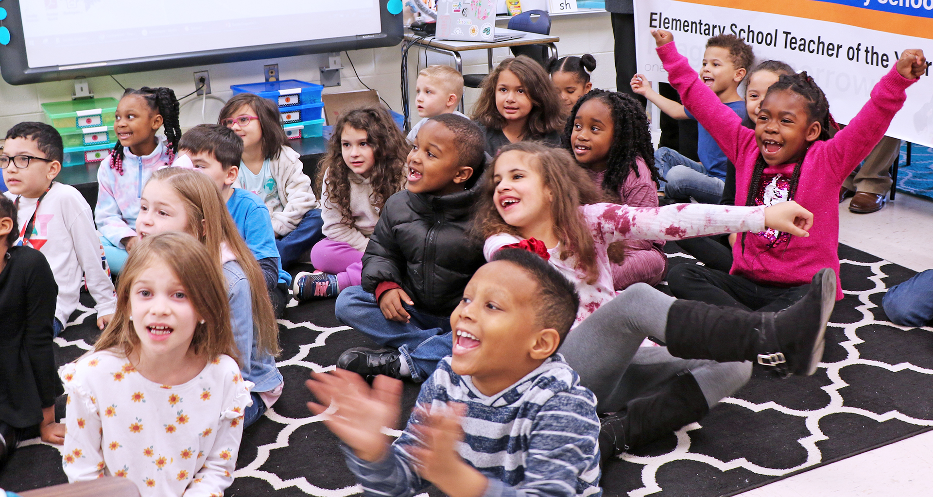 Students on floor in classroom cheering for teacher