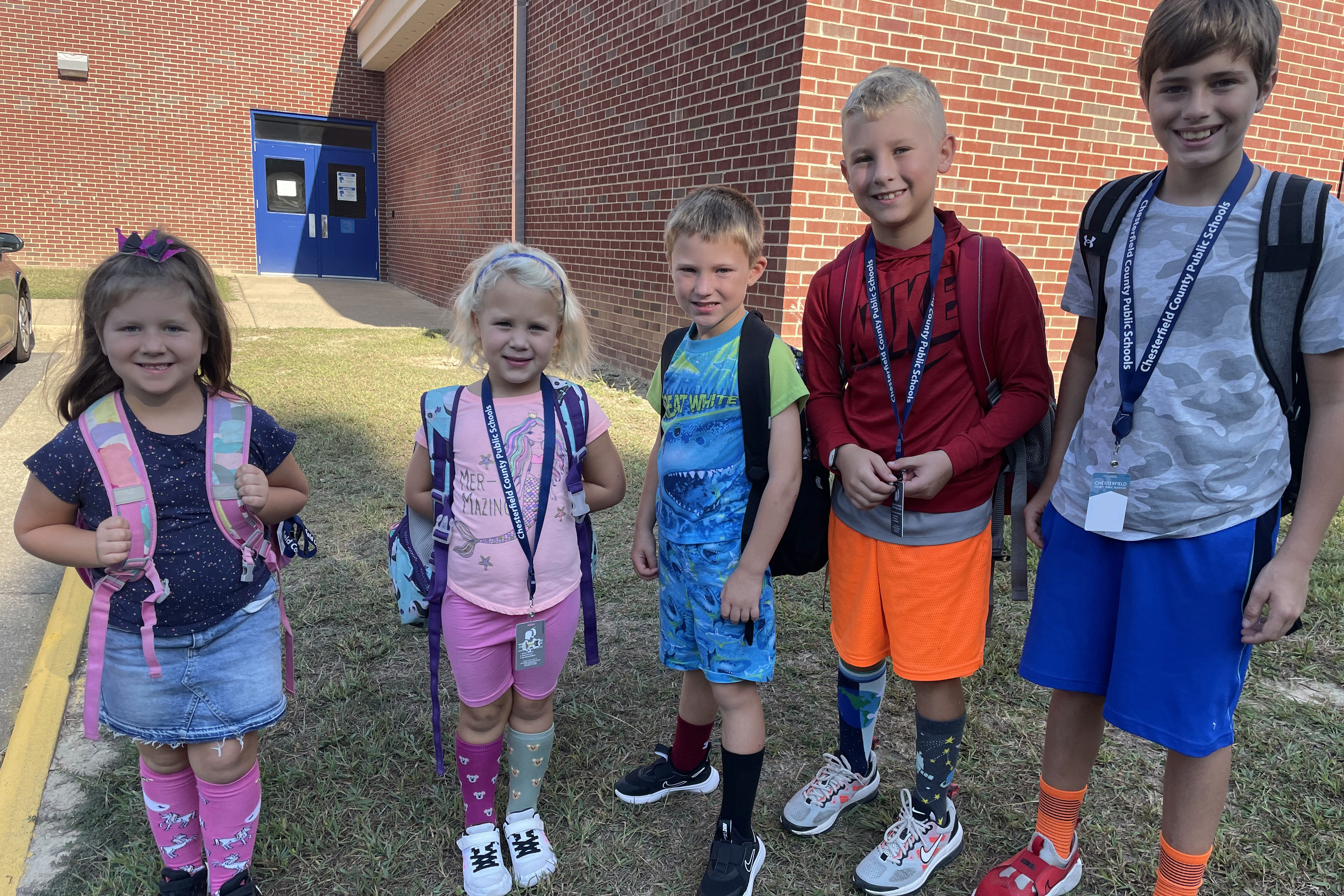 Five students standing outside of the school with their backpacks