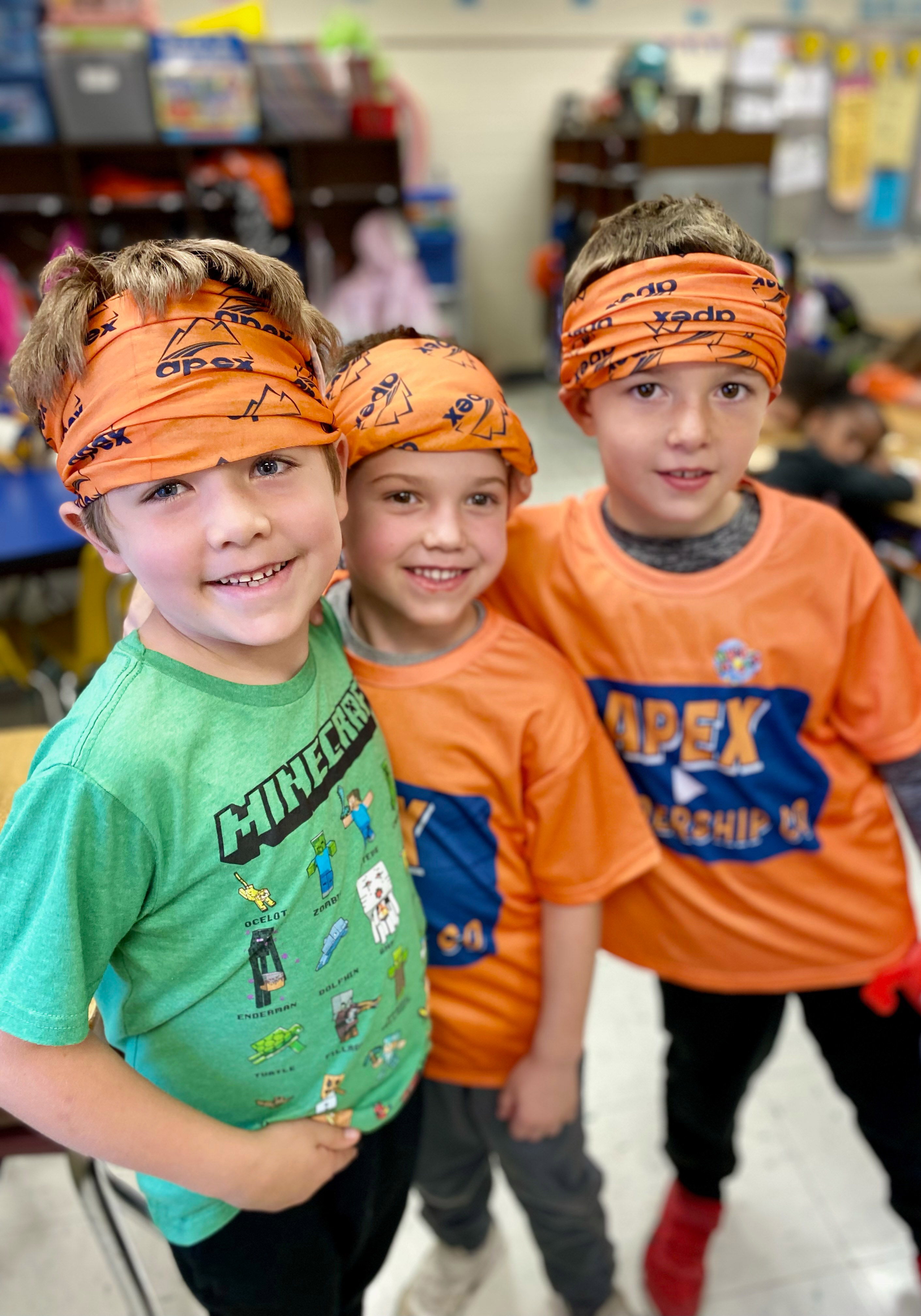 Three students smiling and wearing orange bandanas