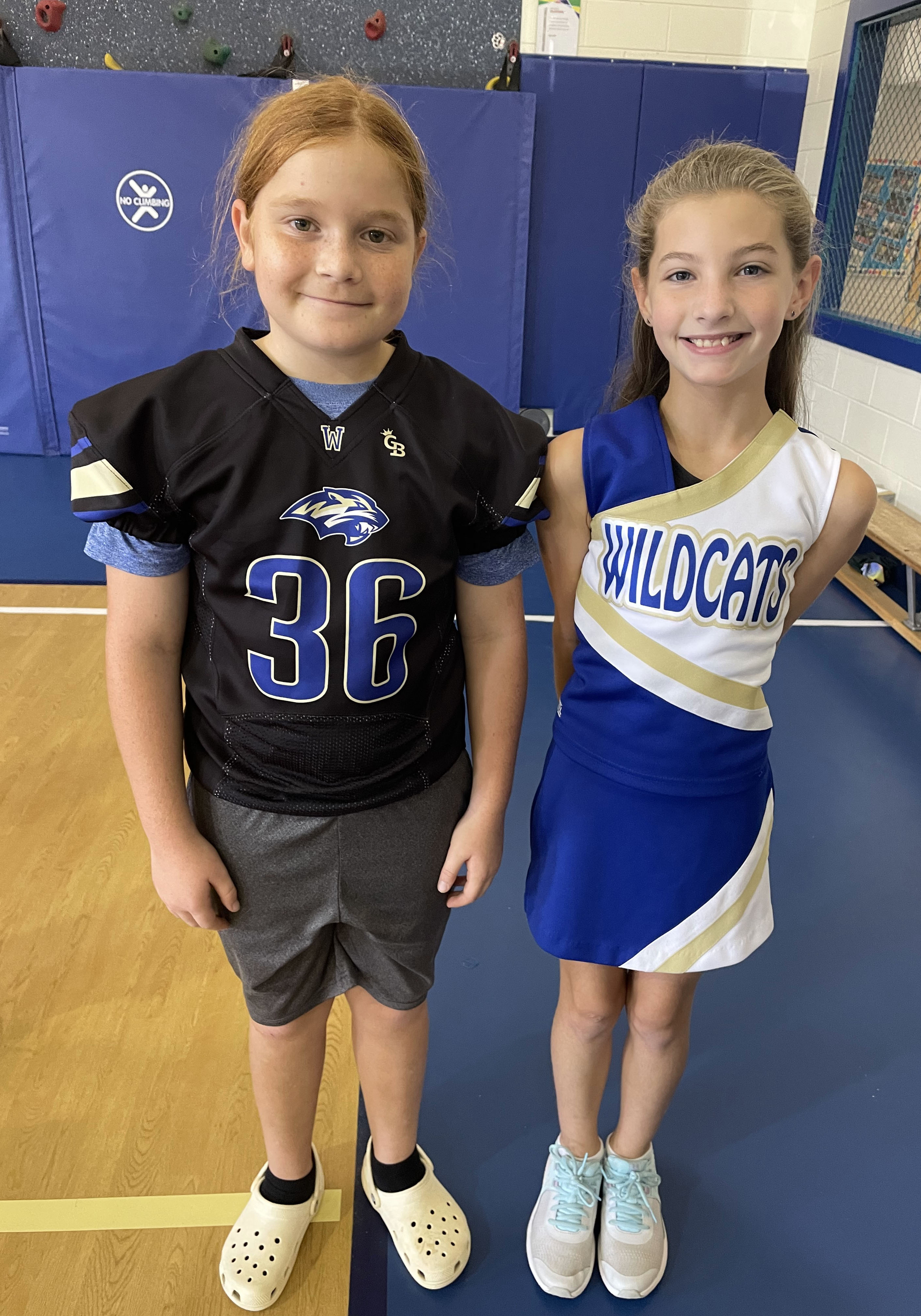 A student wearing a football jersey and another wearing a cheerleader's outfit