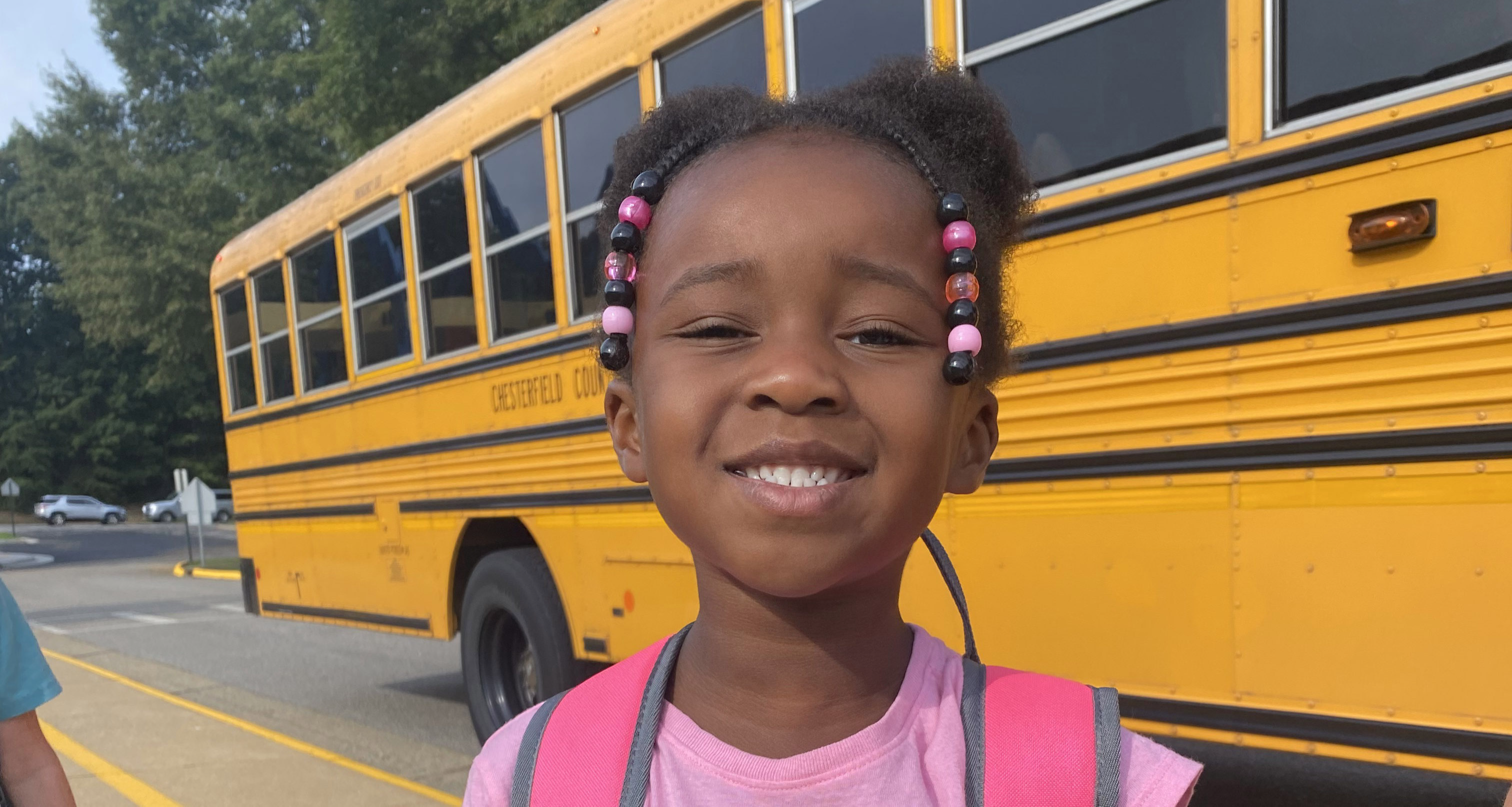 Child smiling in front of a school bus