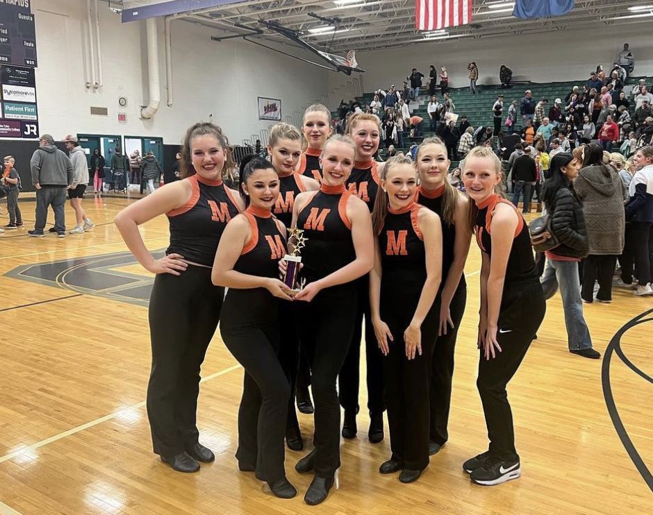 Members of the dance team pose for a photo while one holds a trophy