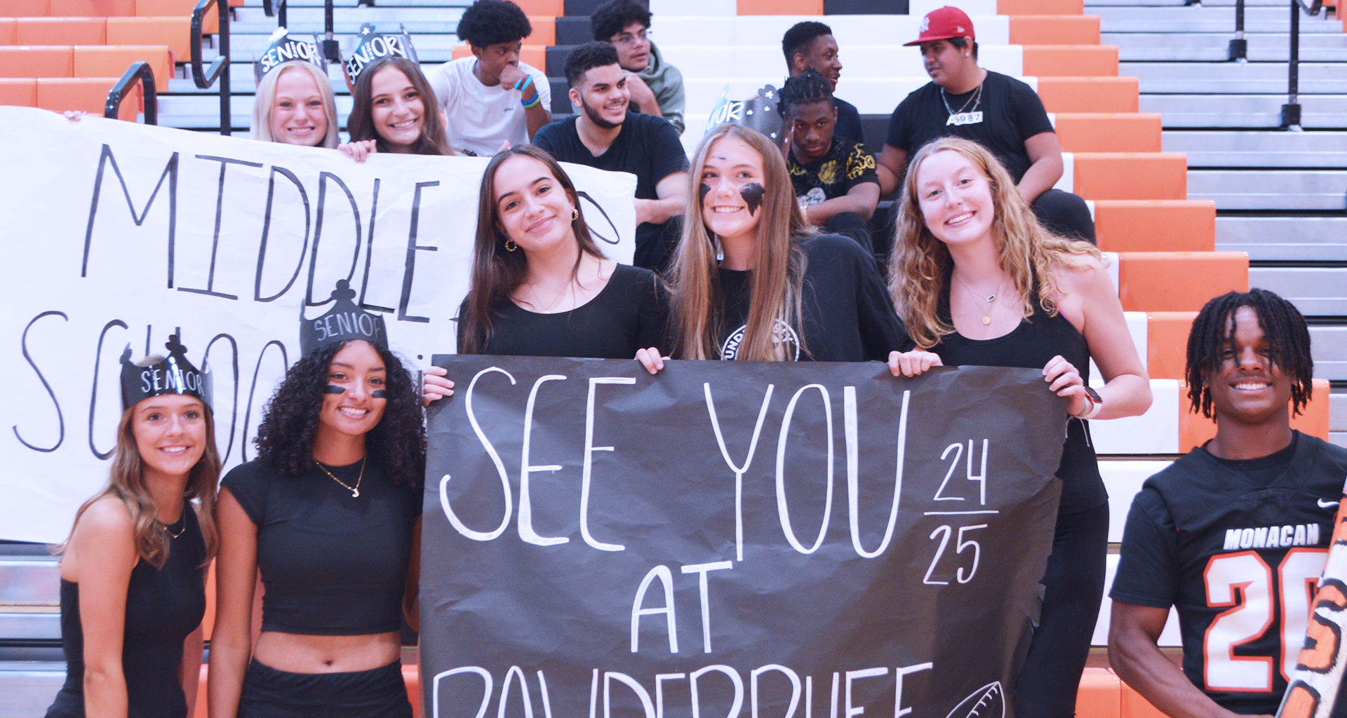 Group of students in gym pose with signs to welcome new students