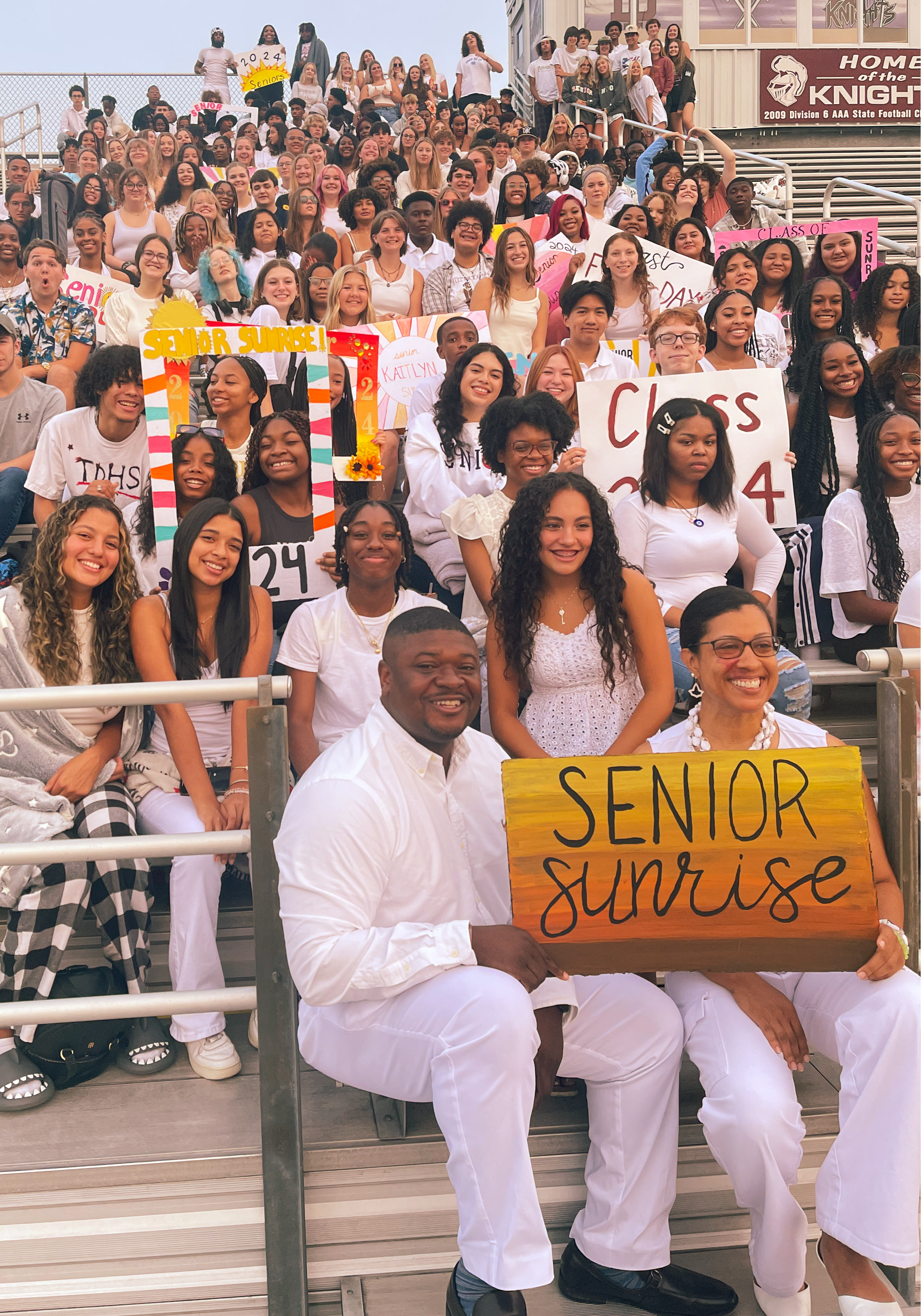 Groupof students and staff sitting in bleachers holding Senior sunrise sign