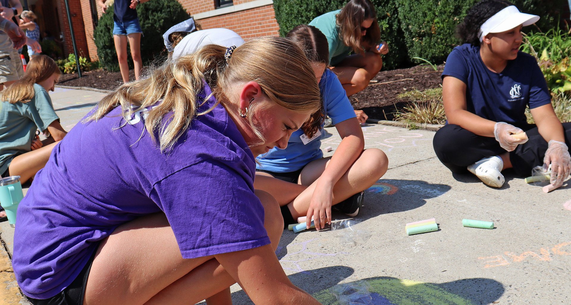 Several students drawing on the sidewalk with chalk