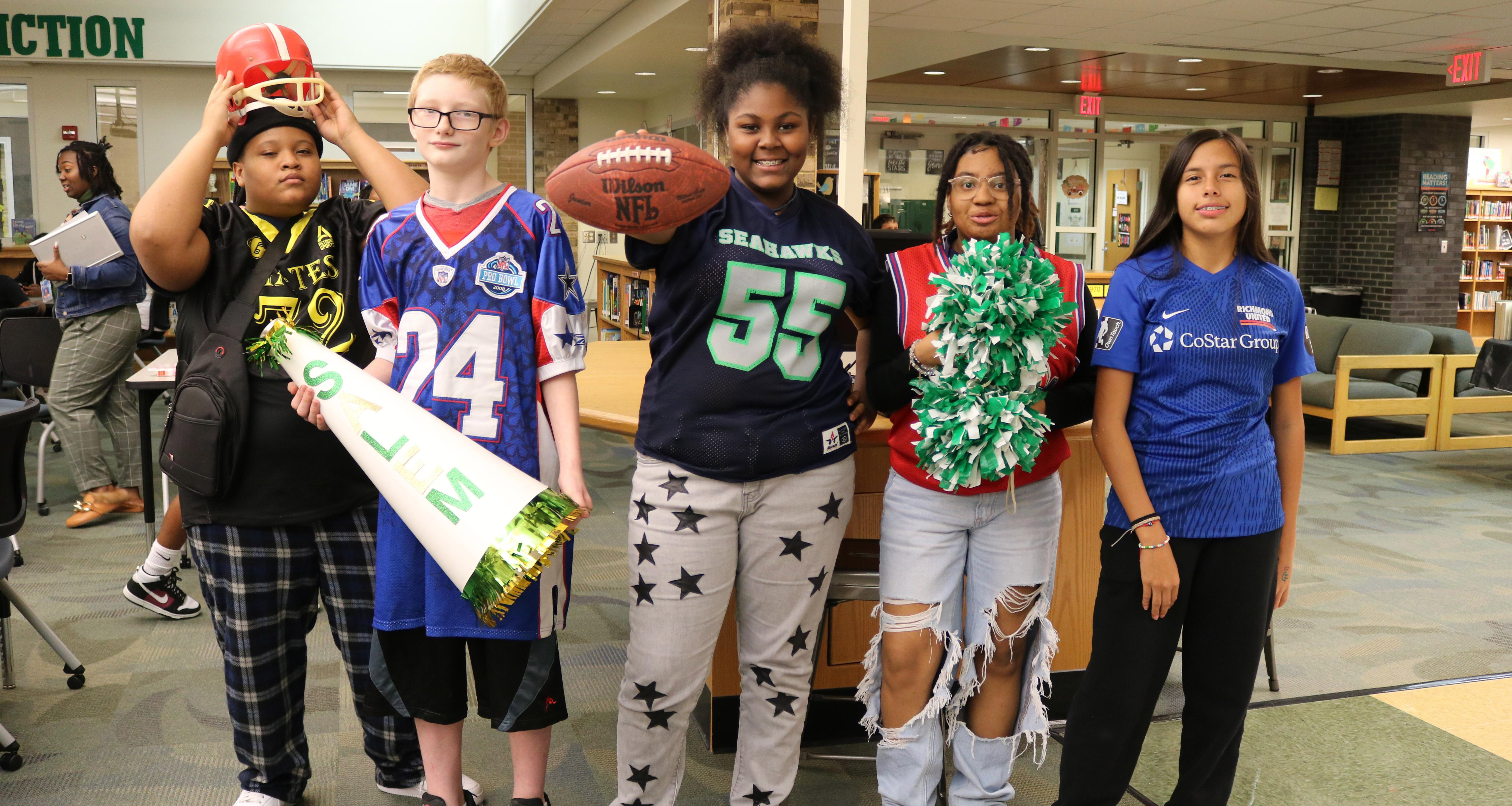 Five students wearing a jersey pose for a photo in the school library