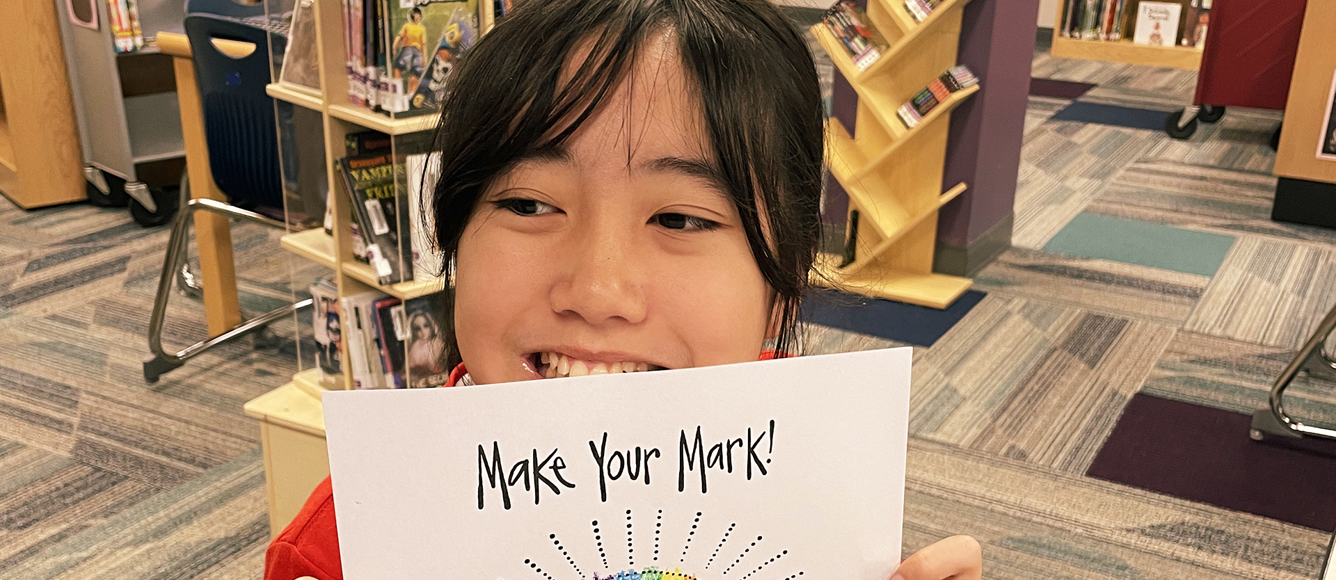 Student holds up artwork that says make your mark