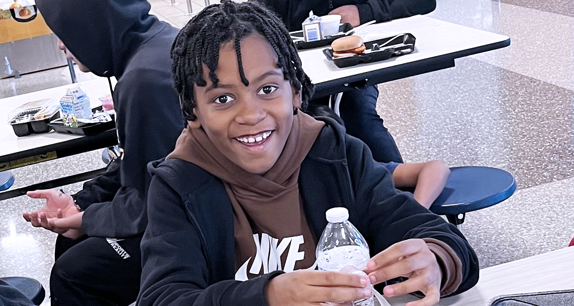 Student sitting in lunch room smiles for a photo