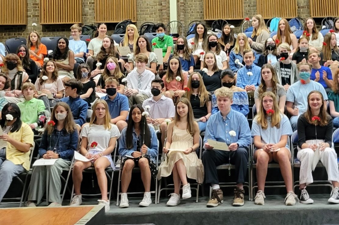 A large group of students sitting on chairs and holding a flower