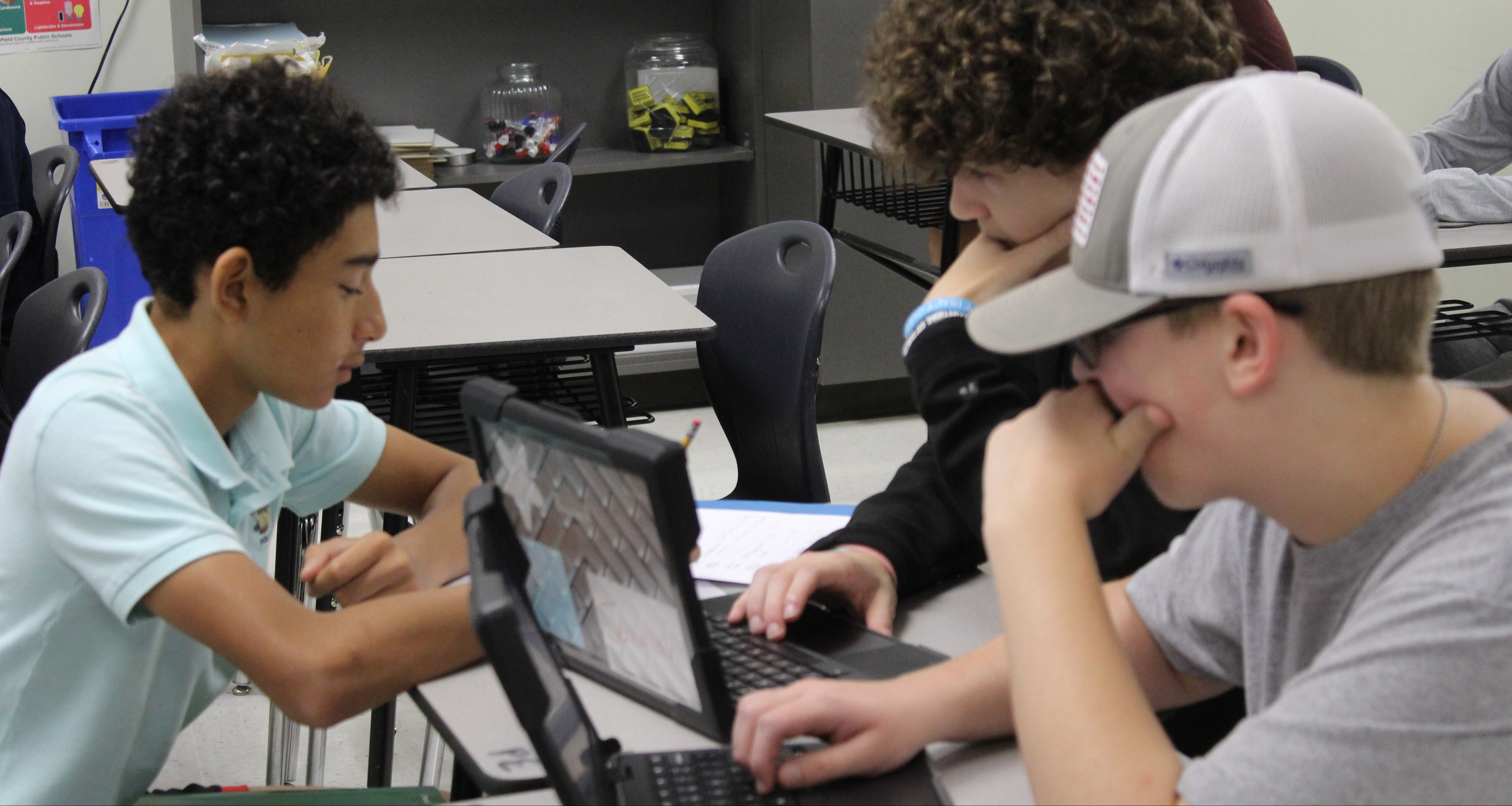Three students focused in class and working on their laptops