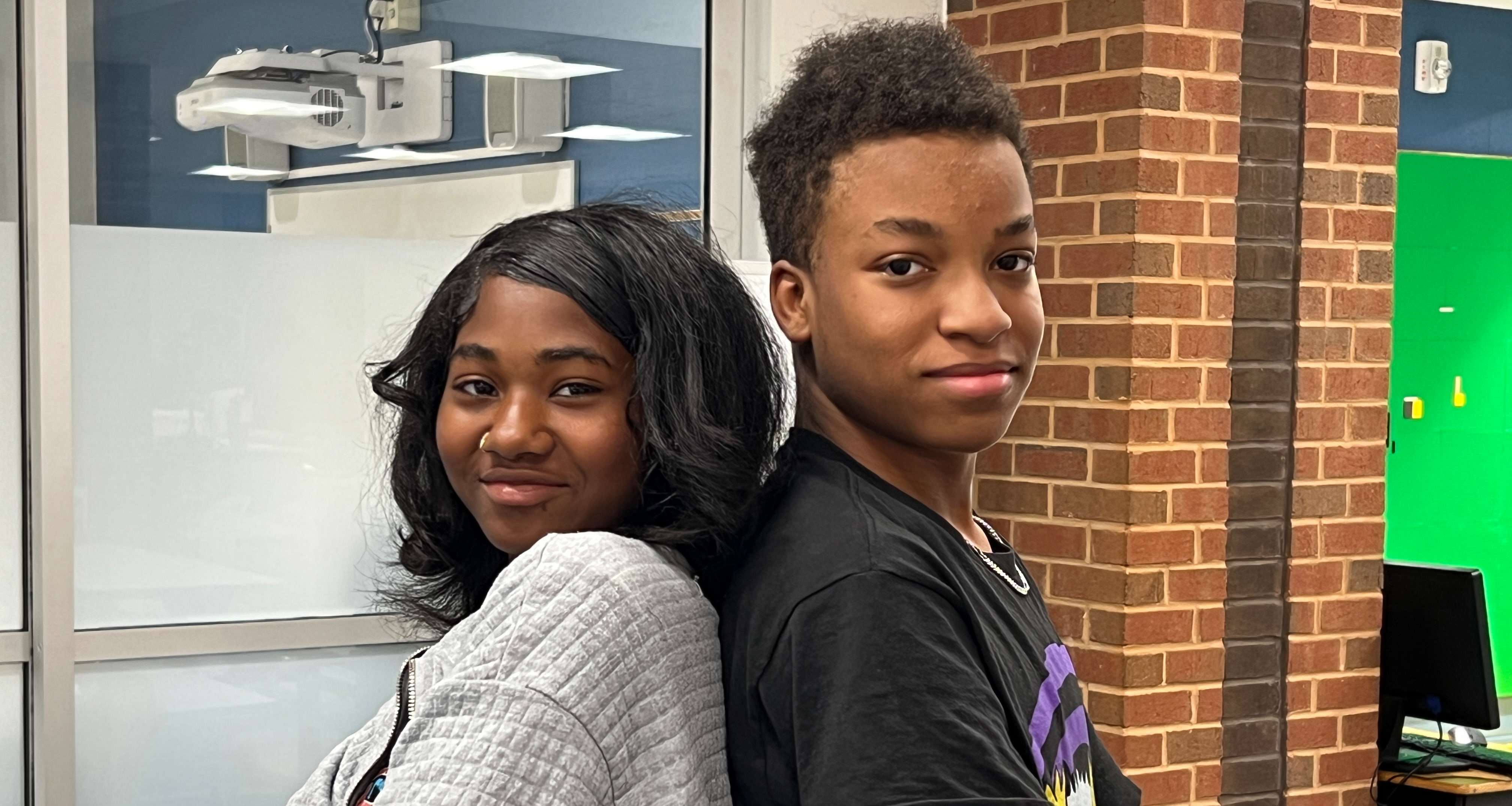 Two students leaning back-to-back posing for a photo
