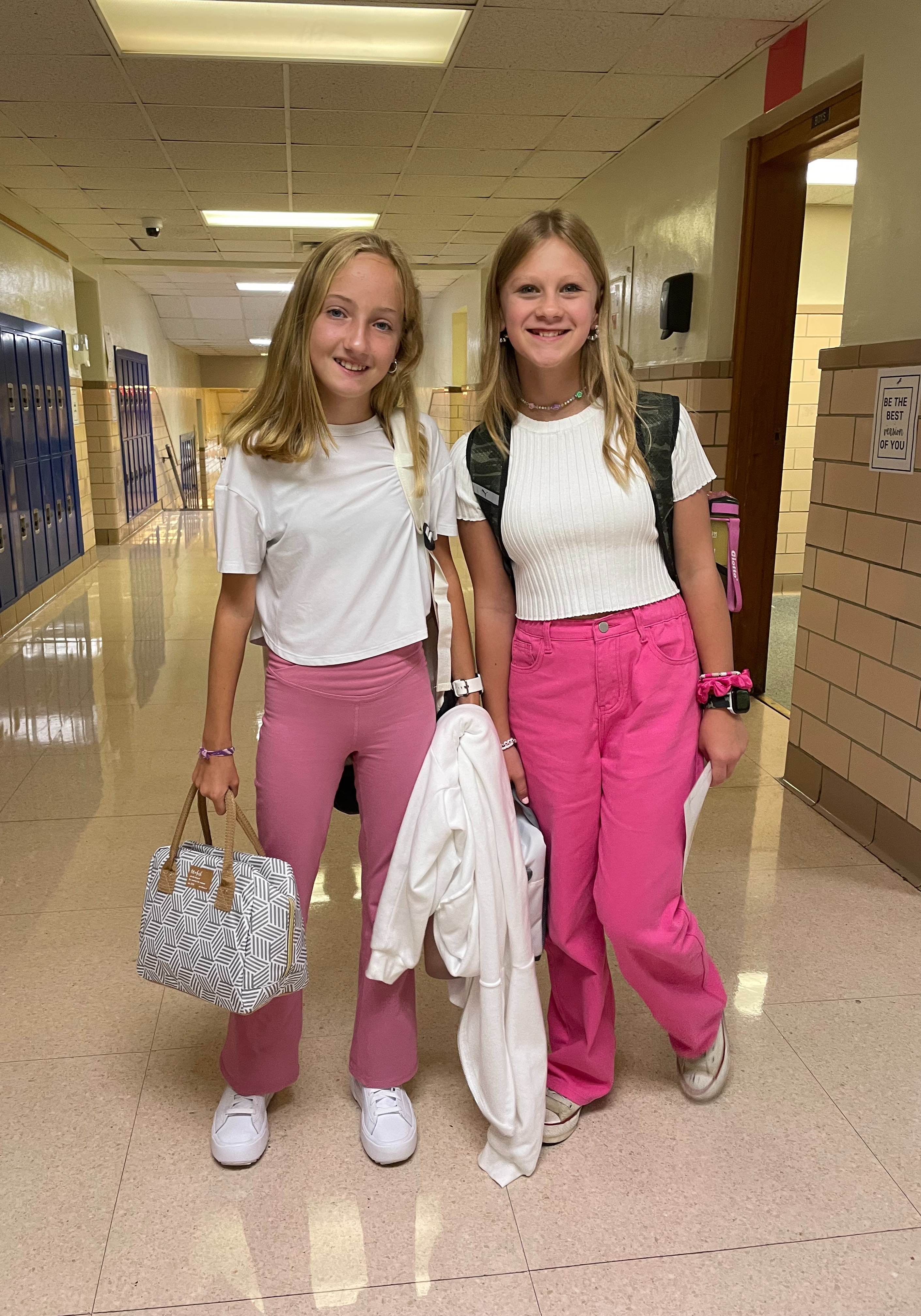 Two girls wearing the same outfit pose for a photo in the hallway