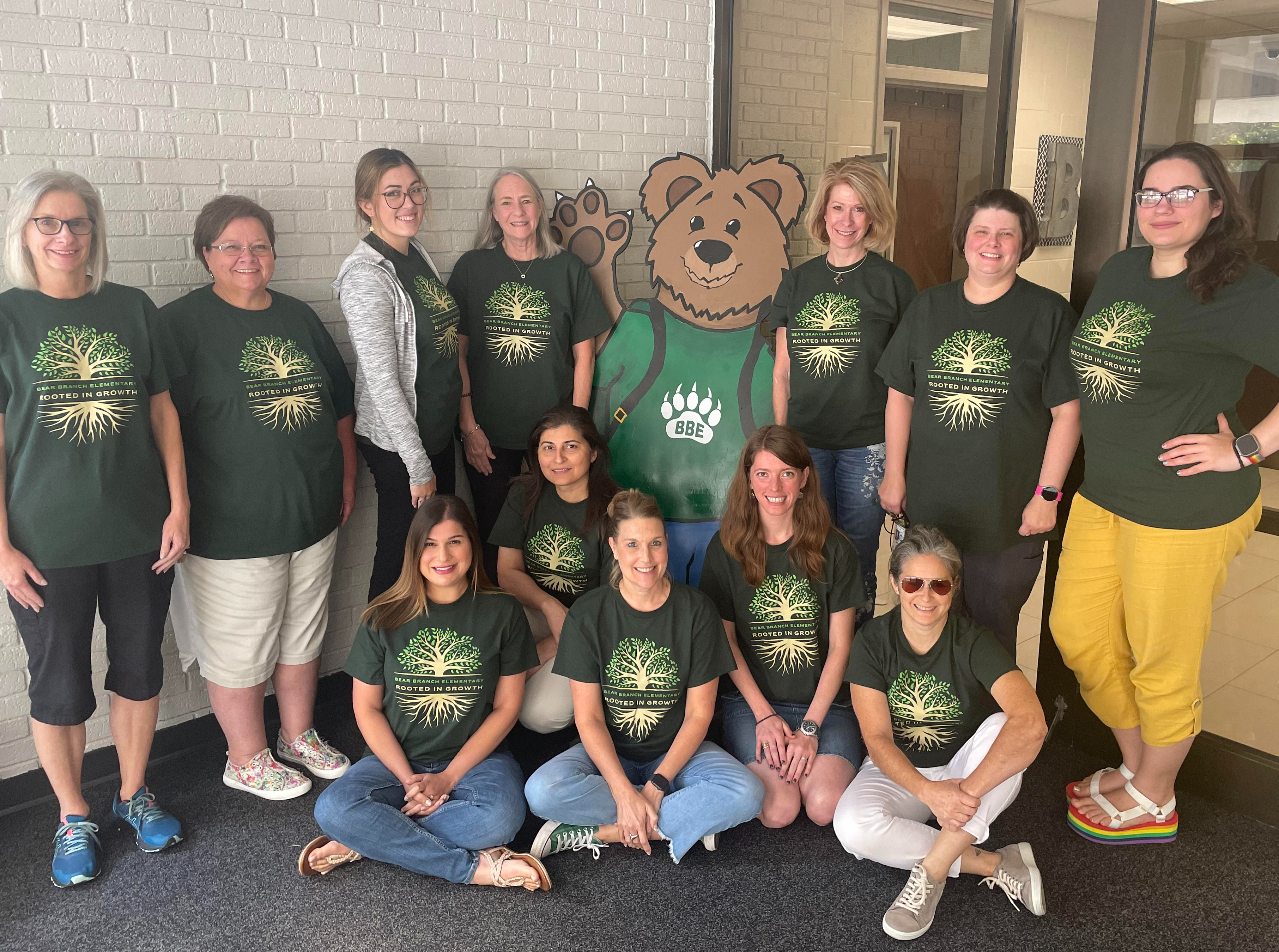 group of teachers in green shirts posing with cartoon bear 