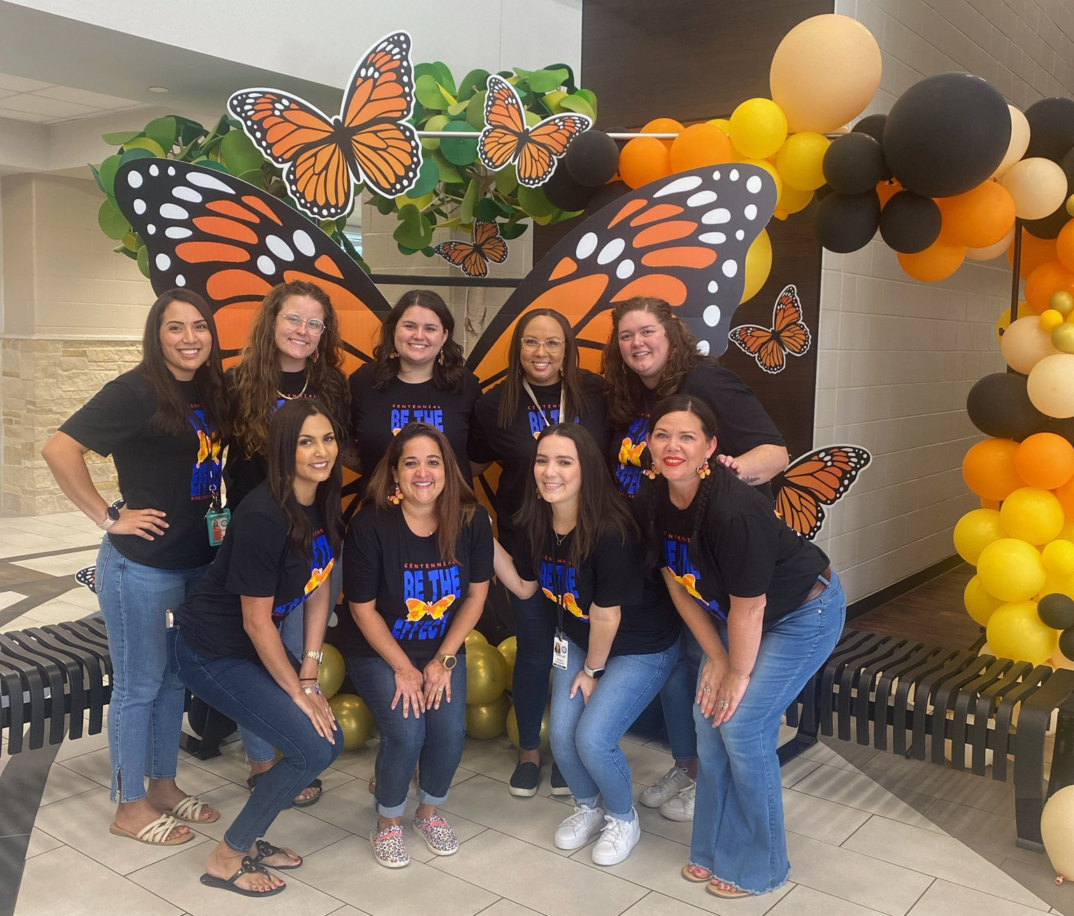 Picture of first grade teachers in black shirts posing with large butterfly backdrop