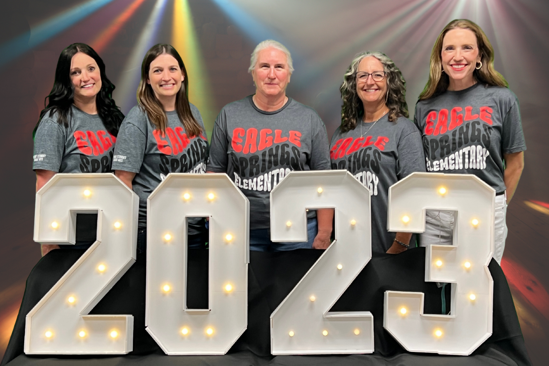 group of teachers in gray shirts standing posing behind lighted 2023 numbers