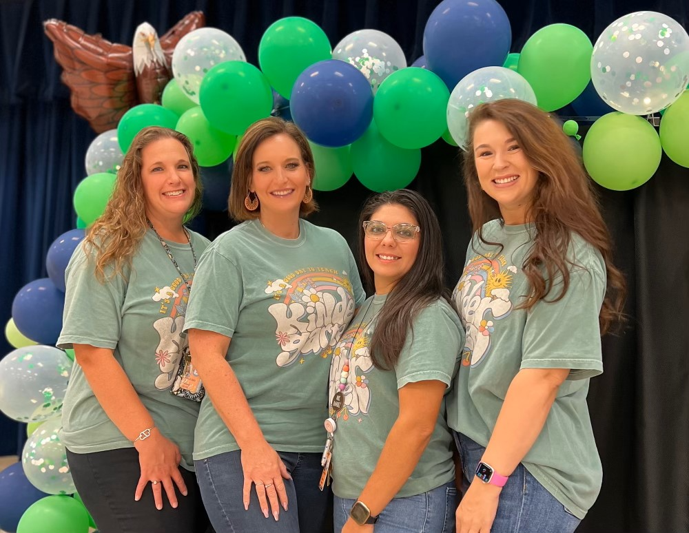 Group of teachers in gray shirts standing posing with balloons