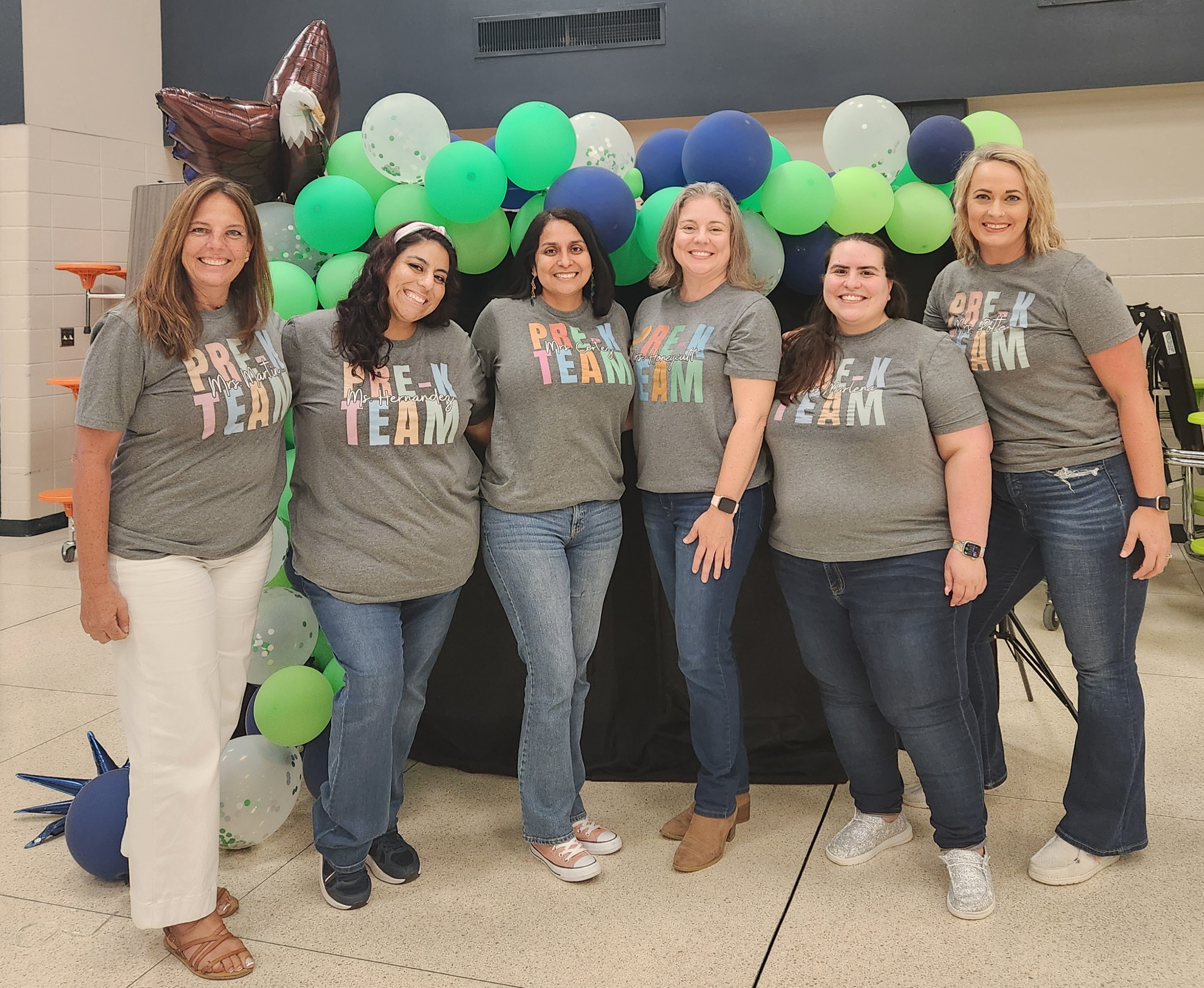 Pre-K teachers in white shirts standing posing in front of green balloons