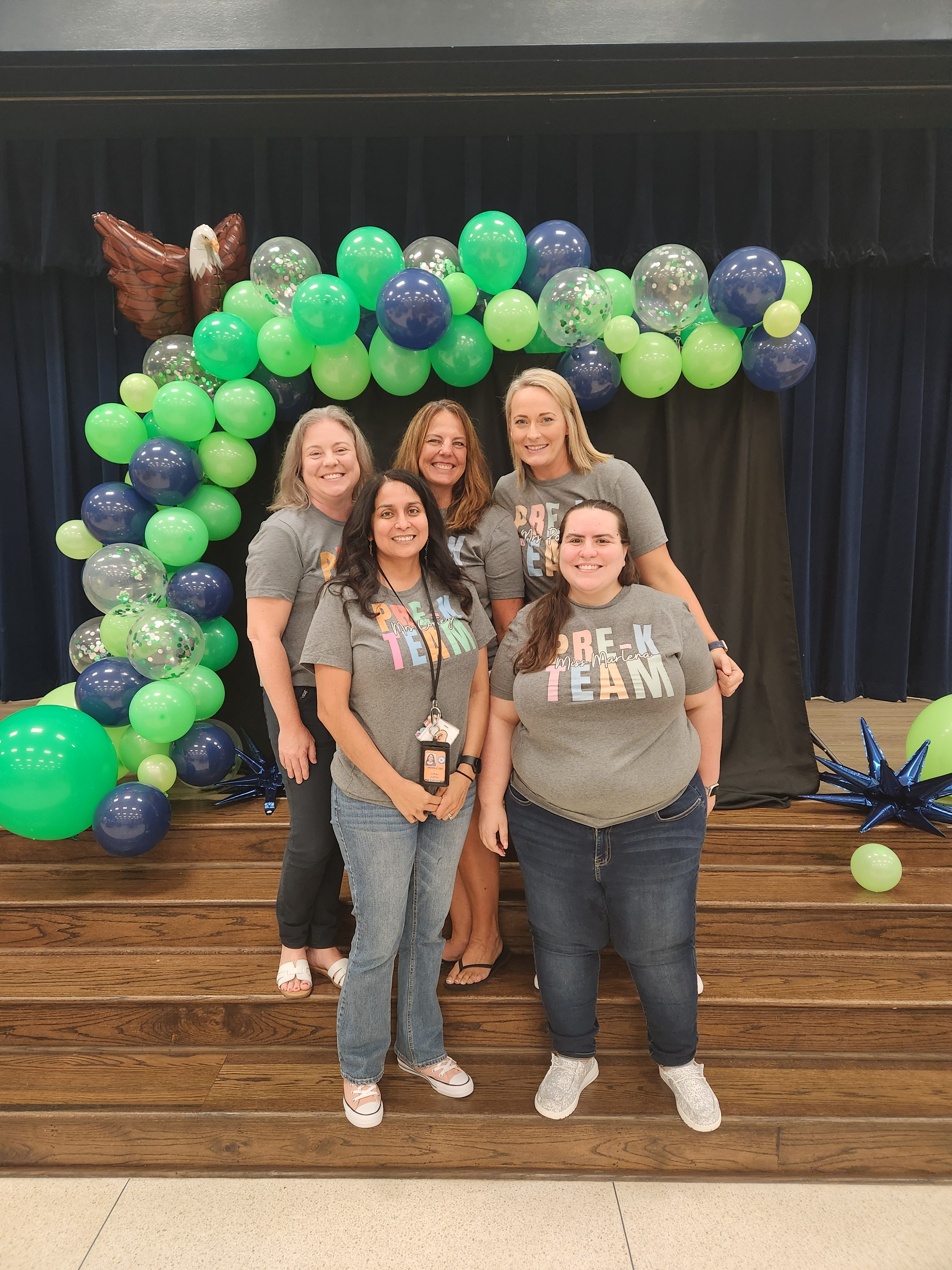 Pre-K teachers in white shirts standing posing in front of green balloons