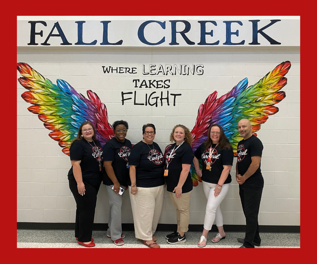 4th grade teachers in black shirts posing in front of wing mural