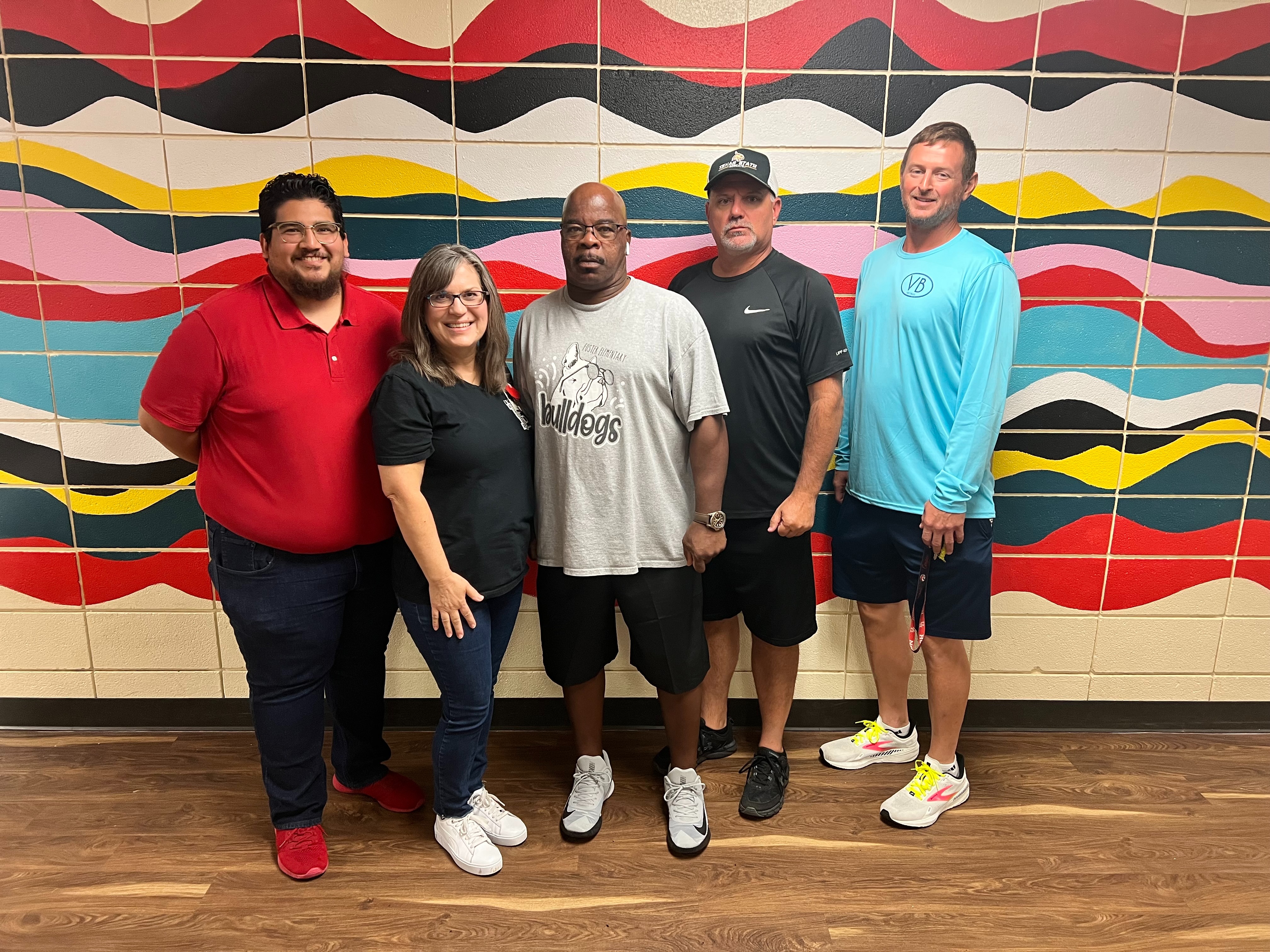 group of 5 people standing in front of colorful wall with waves