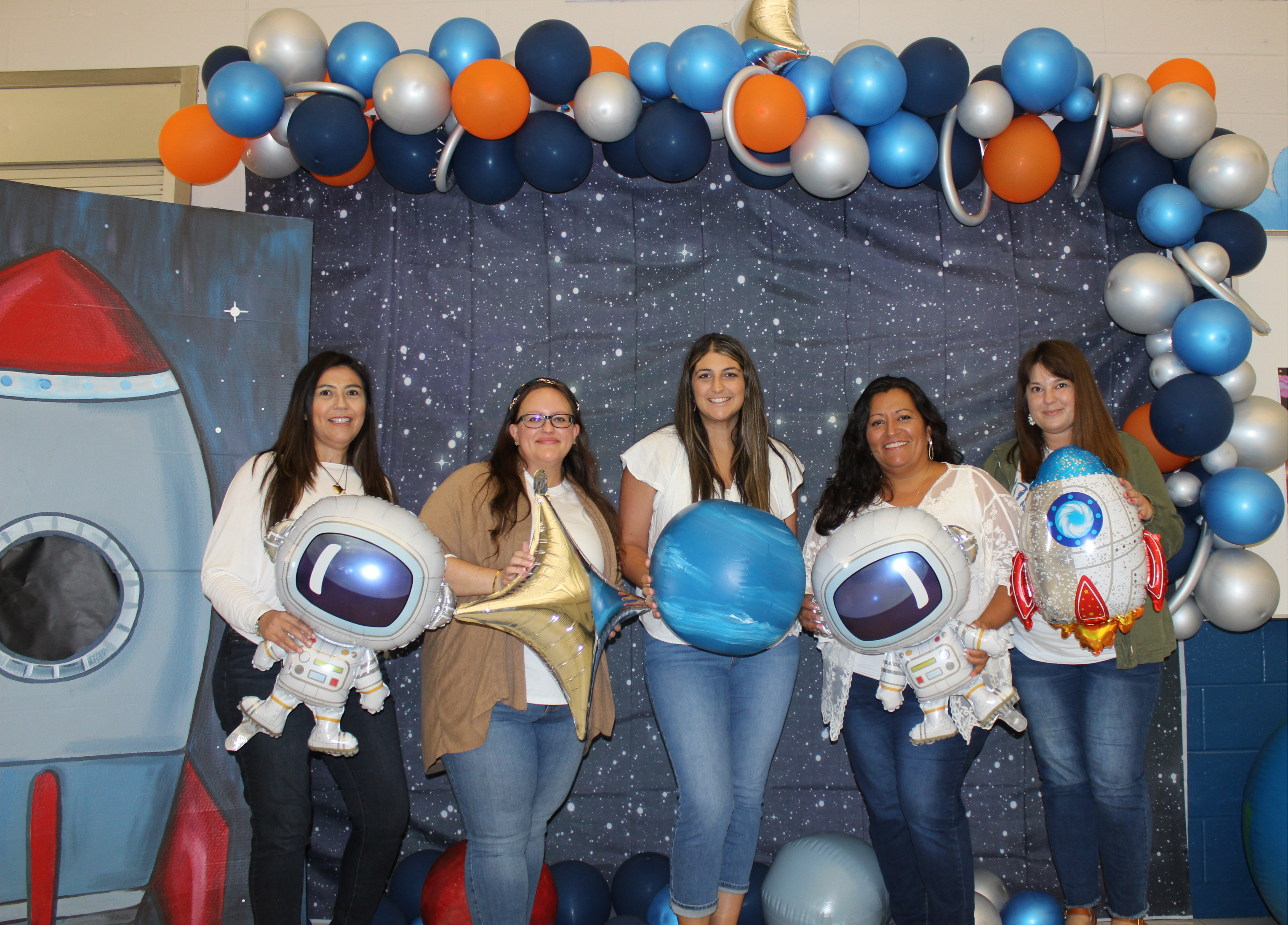 group of 5 people holding balloons posing under ballooons